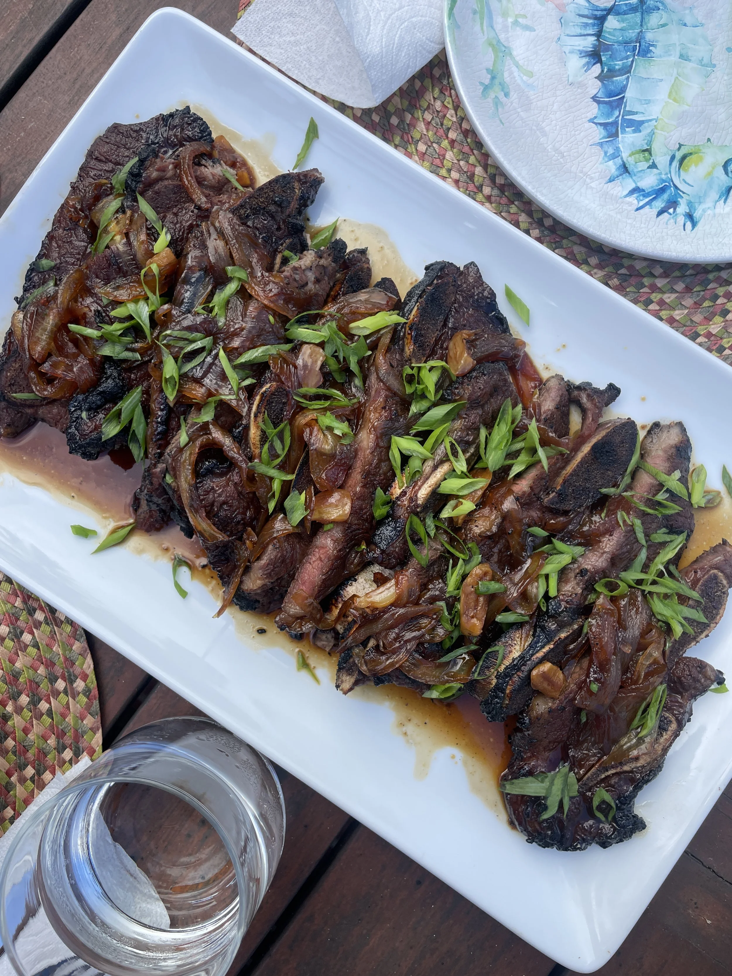 Grilled sliced steak topped with scallions on a white serving platter