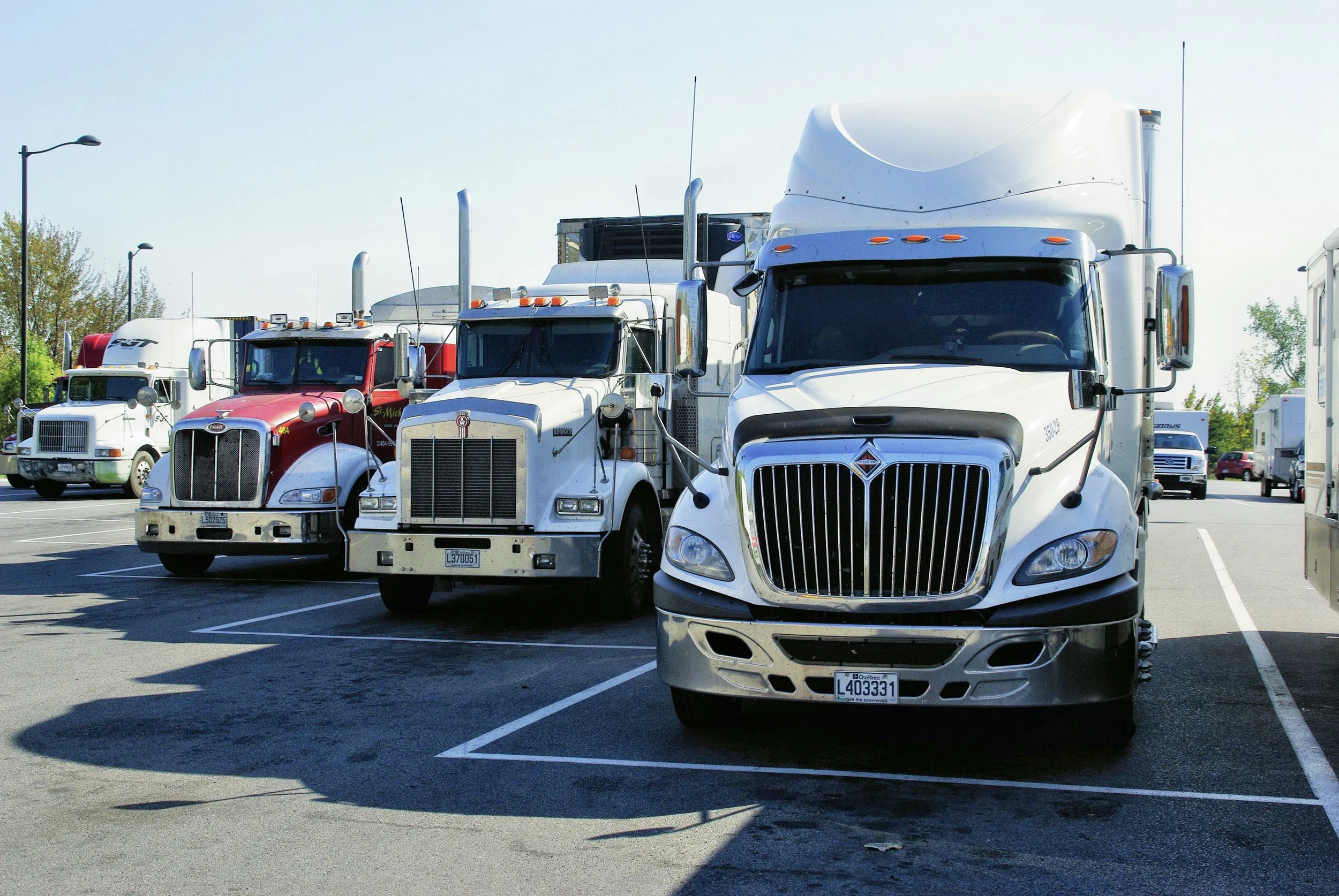 Multiple semi-trucks parked in a parking lot on a sunny day.