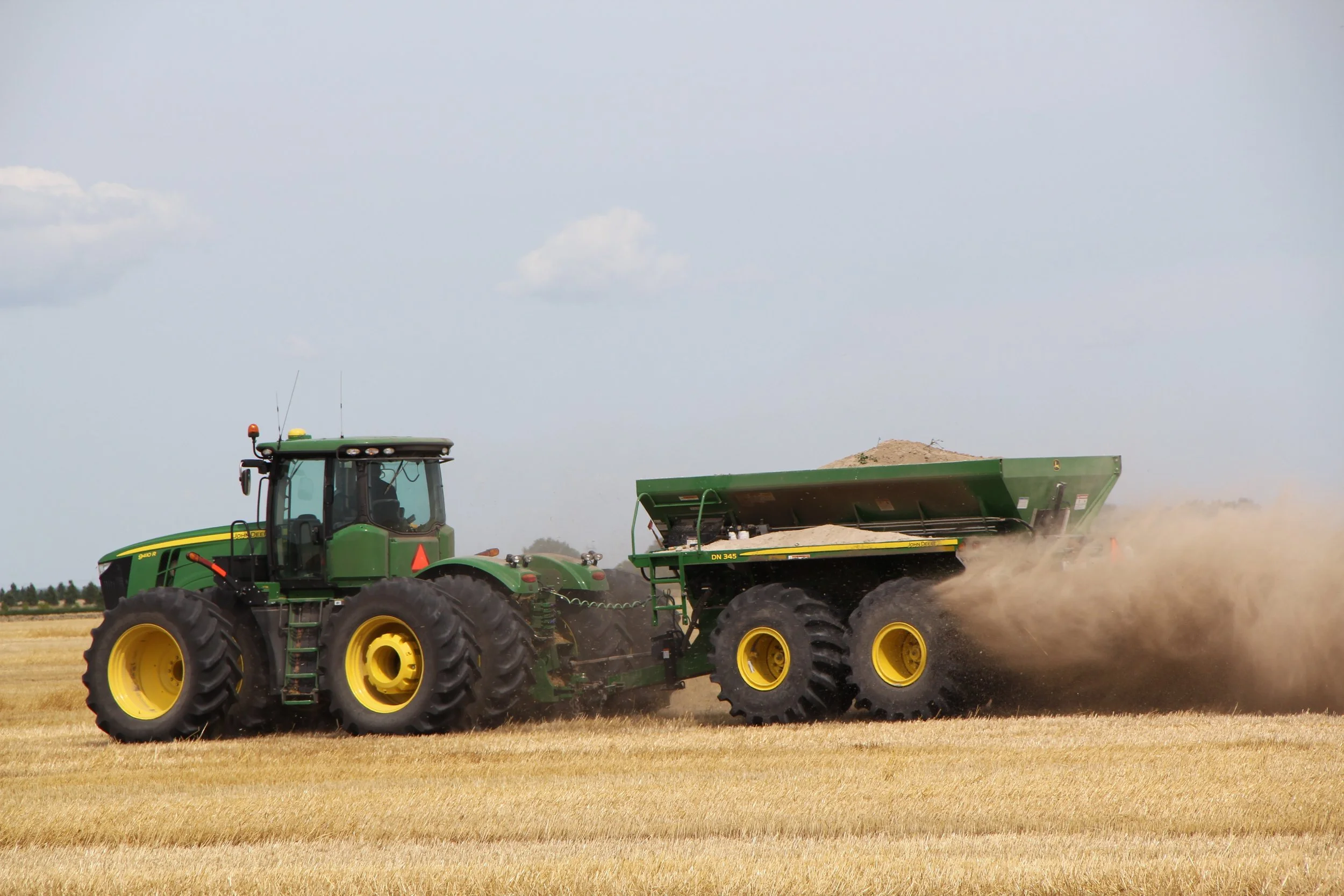 A green tractor with yellow wheels cultivating a field of wheat.
