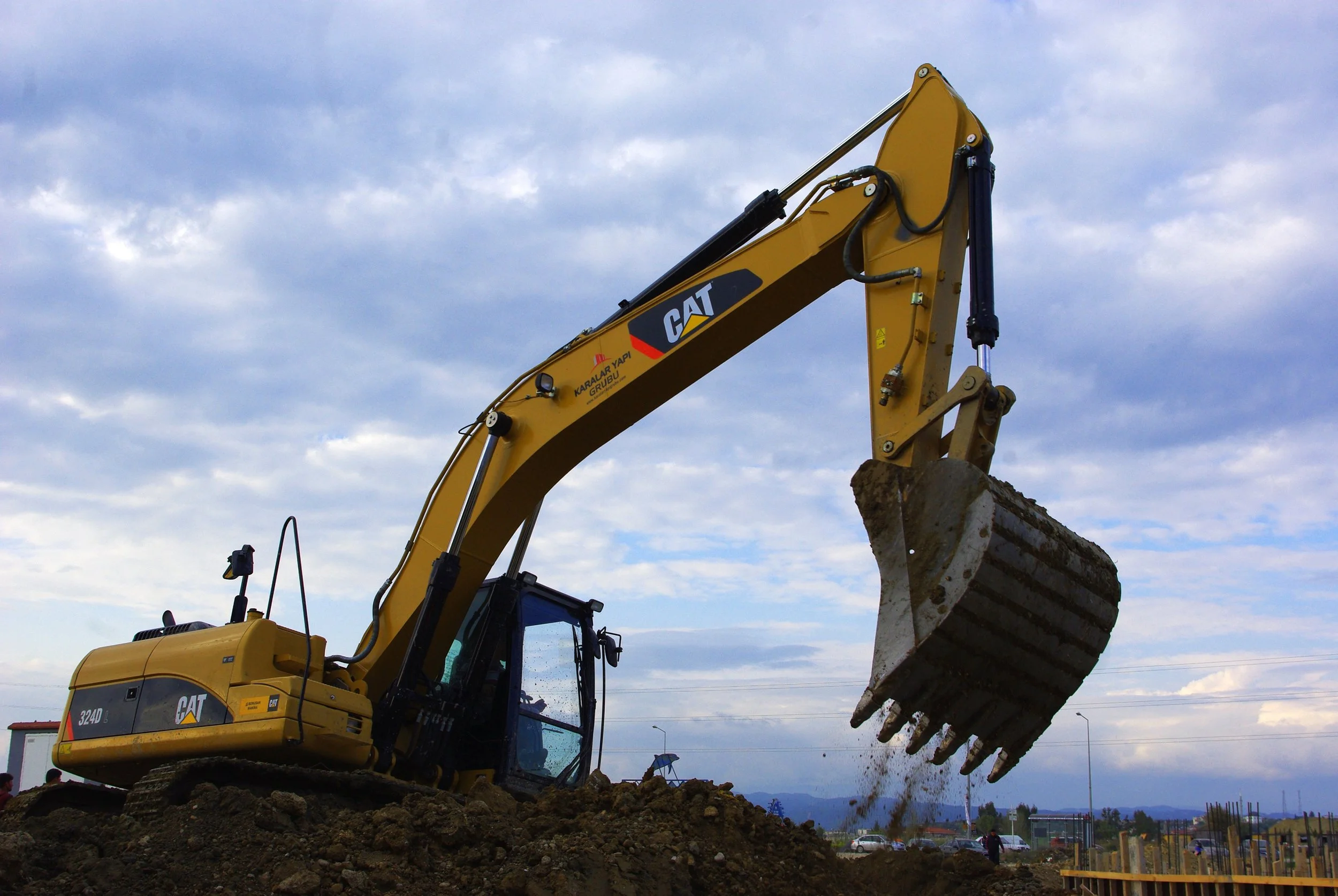 Yellow CAT excavator digging into the dirt at a construction site under a cloudy sky.