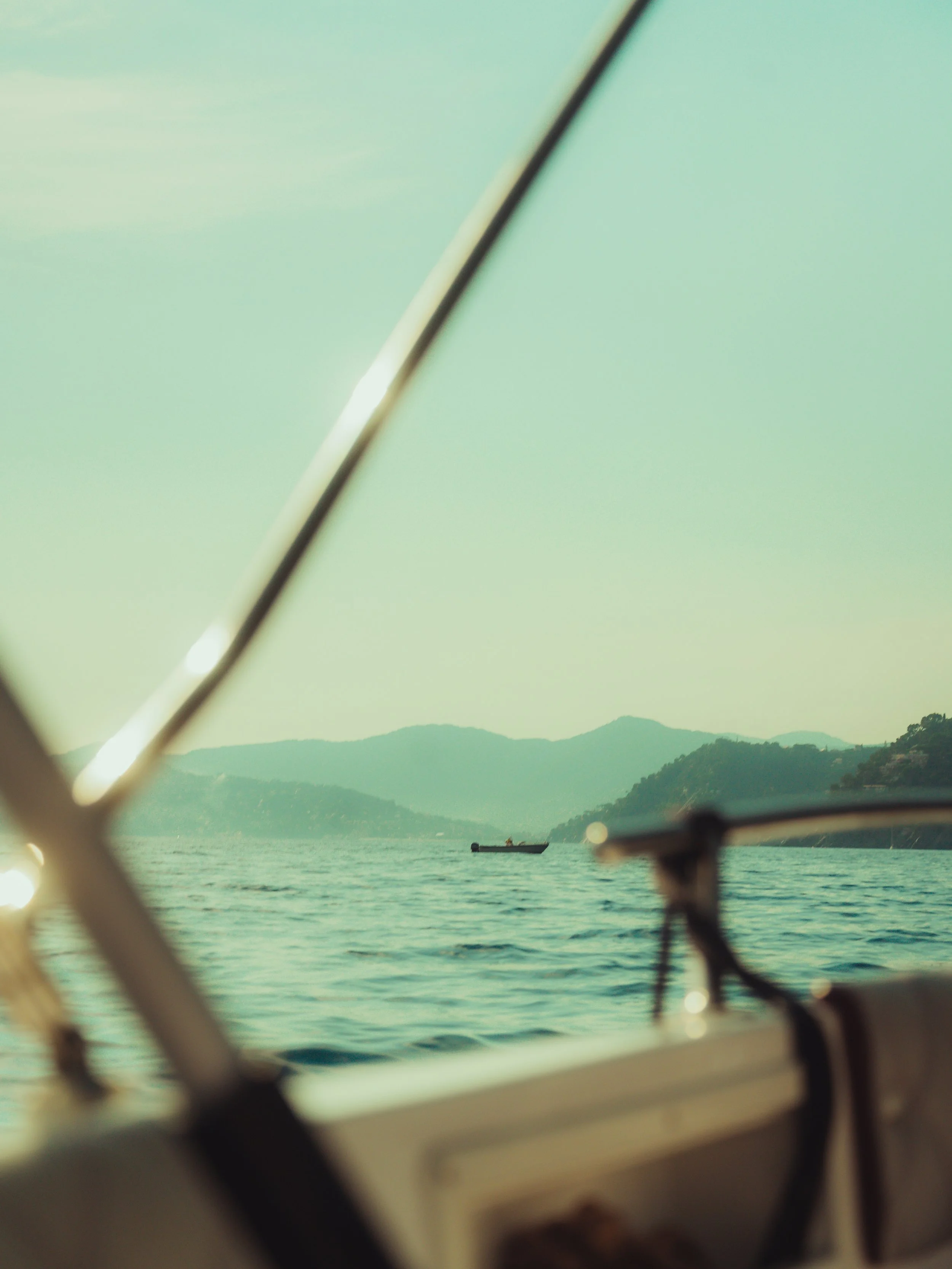 View of a boat on a large body of water, taken from inside another boat through its frame, with distant hills or mountains in the background under a slightly cloudy sky.
