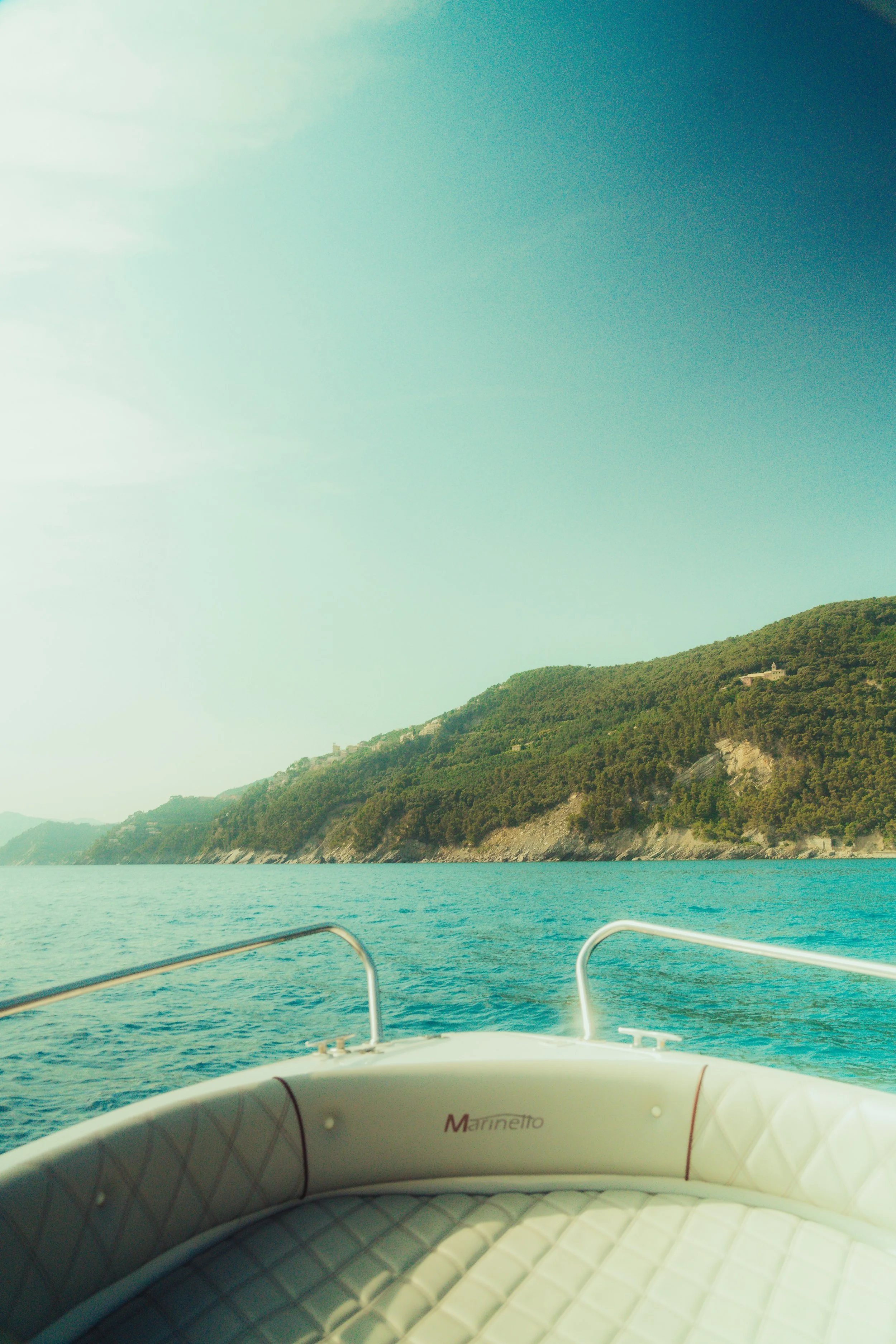 View from a boat on a body of water facing a hillside with trees and a house. The boat's interior is visible in the foreground.