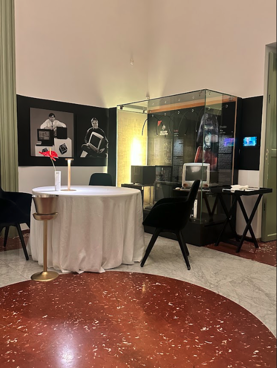 A table and chairs in a restaurant. There are photos of Steve Jobs and computers on the walls, and an old computer sits in a display case.