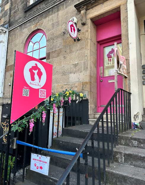 A pink sign and pink door advertising the Chihuahua Cafe, and a short flight of stone steps.