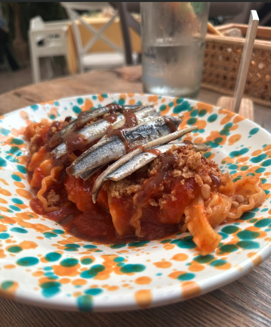 A dish of pasta with tomato sauce, bread crumbs, and anchovies, on a green and orange speckled dish.