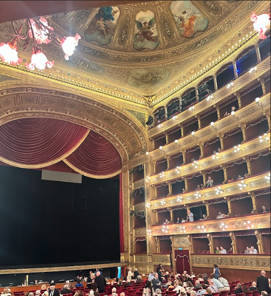 The interior of an opera house, with red curtains and gold interior.