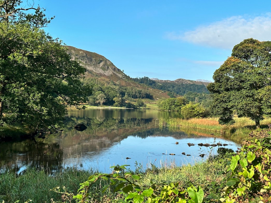 A beautiful lake sits among vibrant green landscape and rolling hills.
