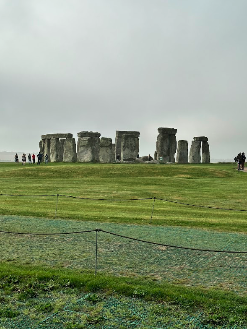 A photo of Stonehenge from behind ropes. Large stones placed in circles and horseshoes.