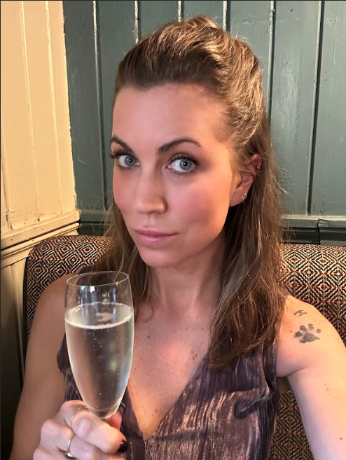 A woman in a dusty rose-colored velvet dress smiles and holds a glass of champagne.