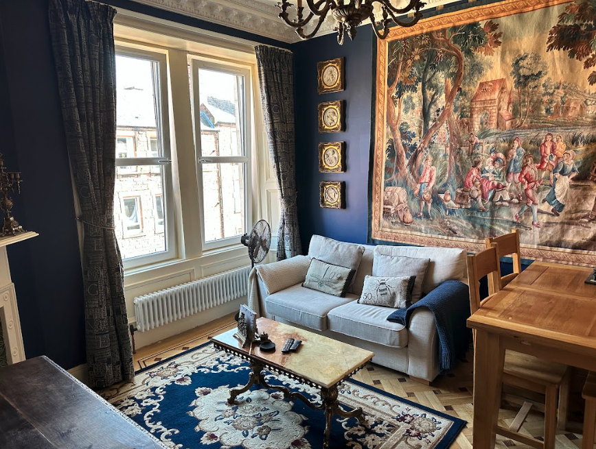 A living room with dark blue walls, a large tapestry, and large windows overlooking a city.