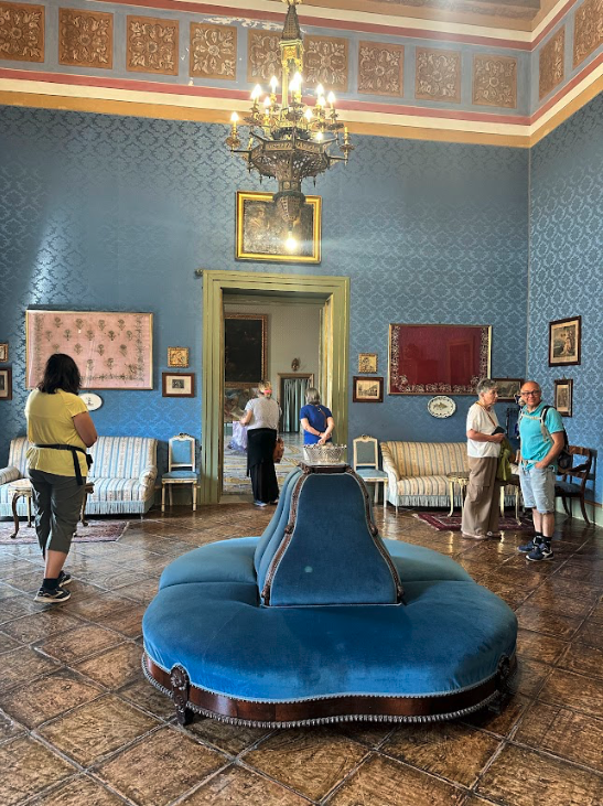 A room in a palace with opulent decor and a blue velvet circular sofa.