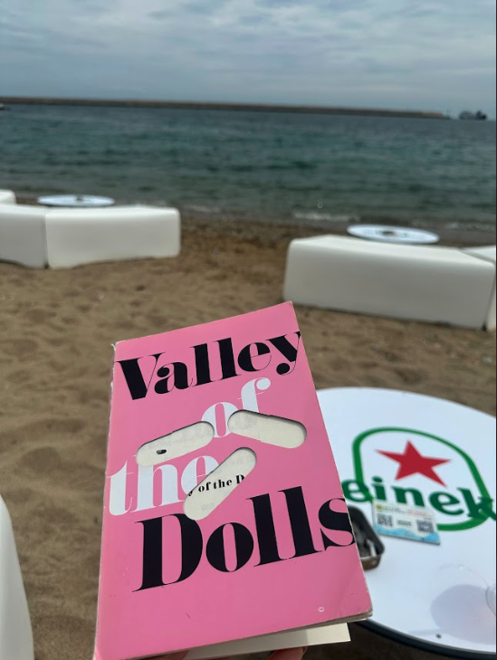 A book with tables in the background on a beach, there is a body of water in the background.