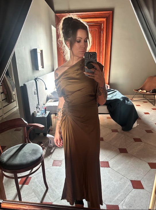 A woman stands in front of a mirror wearing a bronze gown.