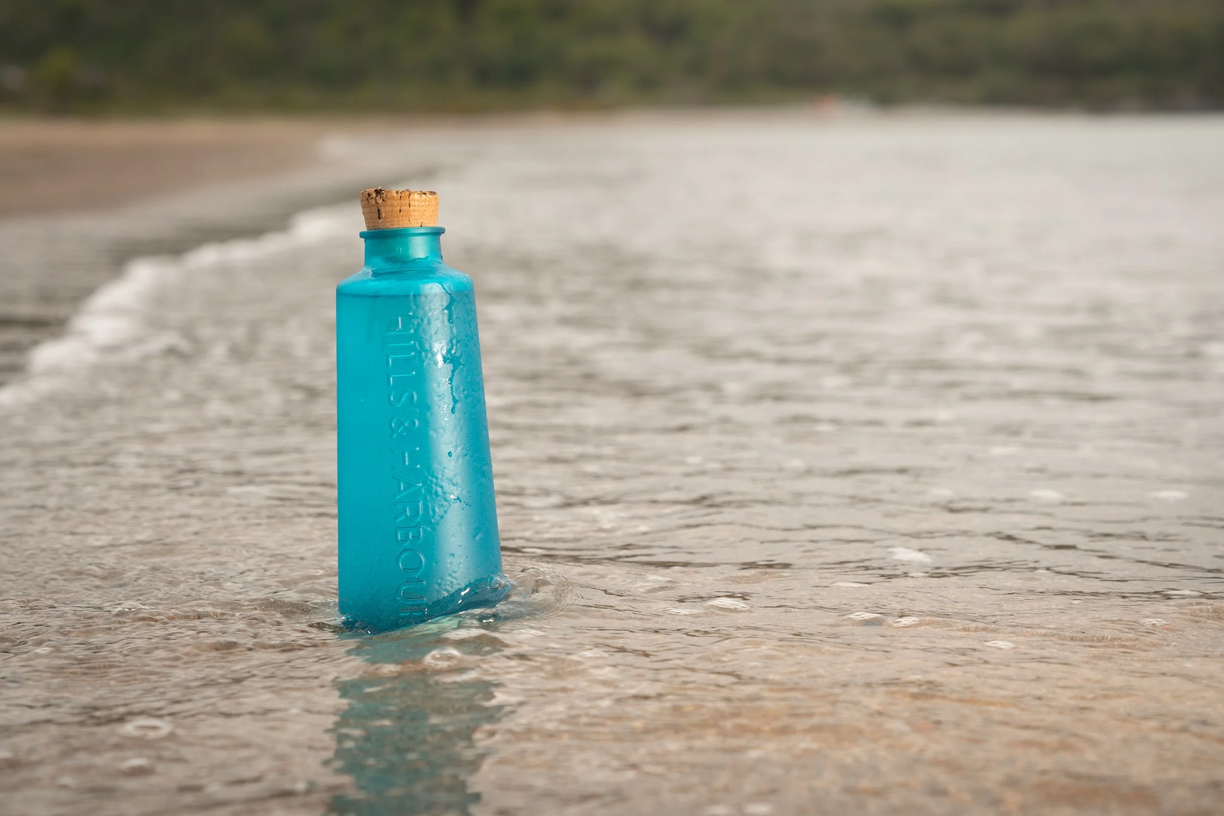 A bottle of Hills and Harbour Gin in the sea at the beach