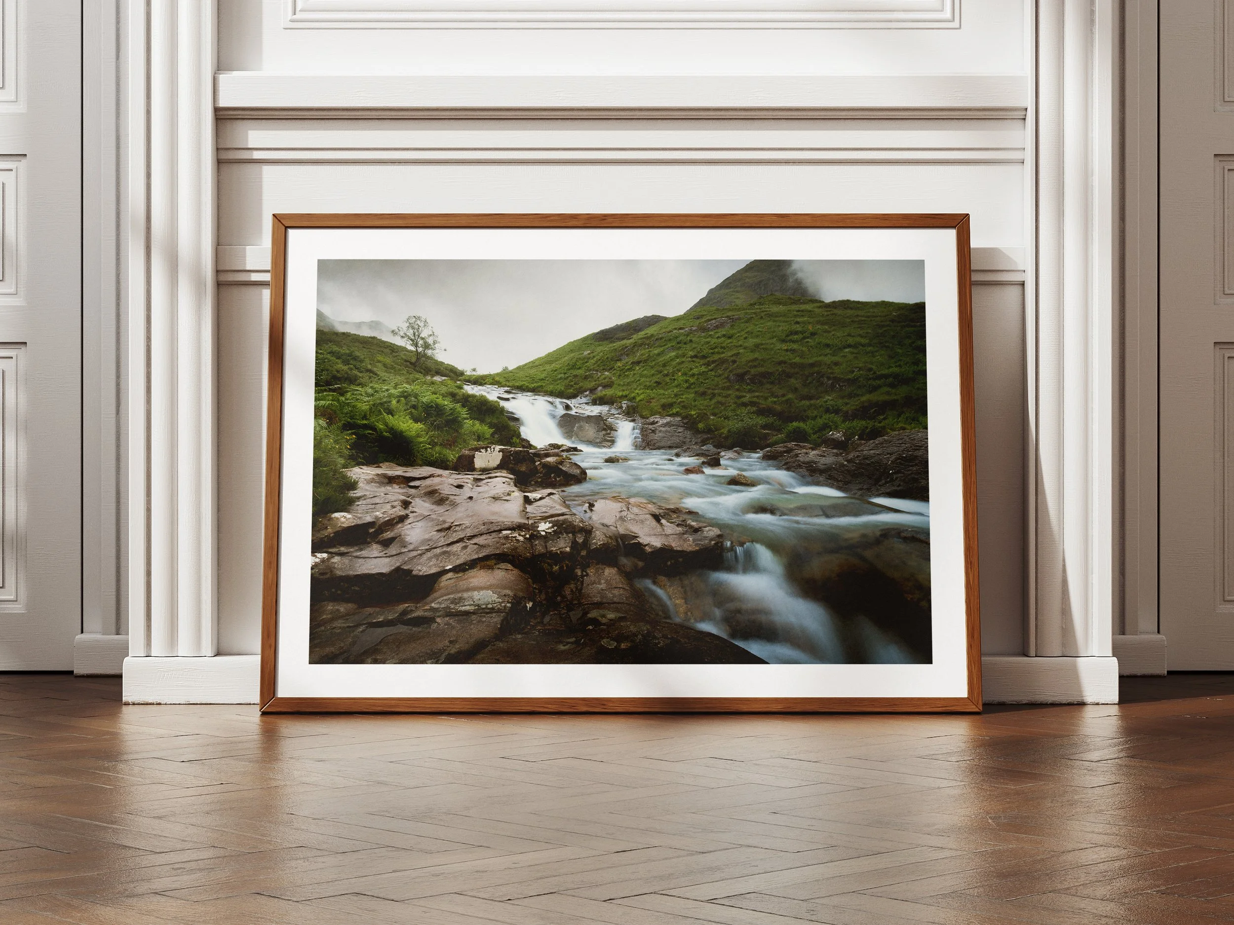 A framed picture of a river flowing through moody mountains
