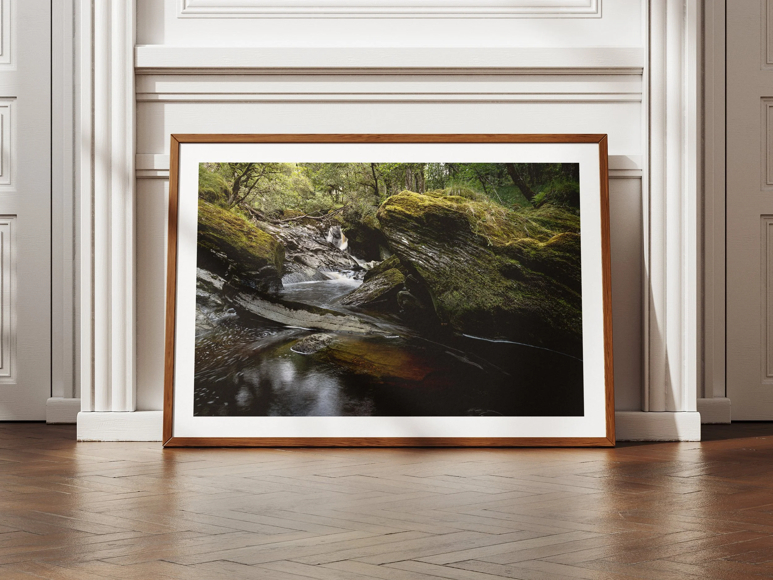A framed picture of a river flowing through rocks deep in a forest