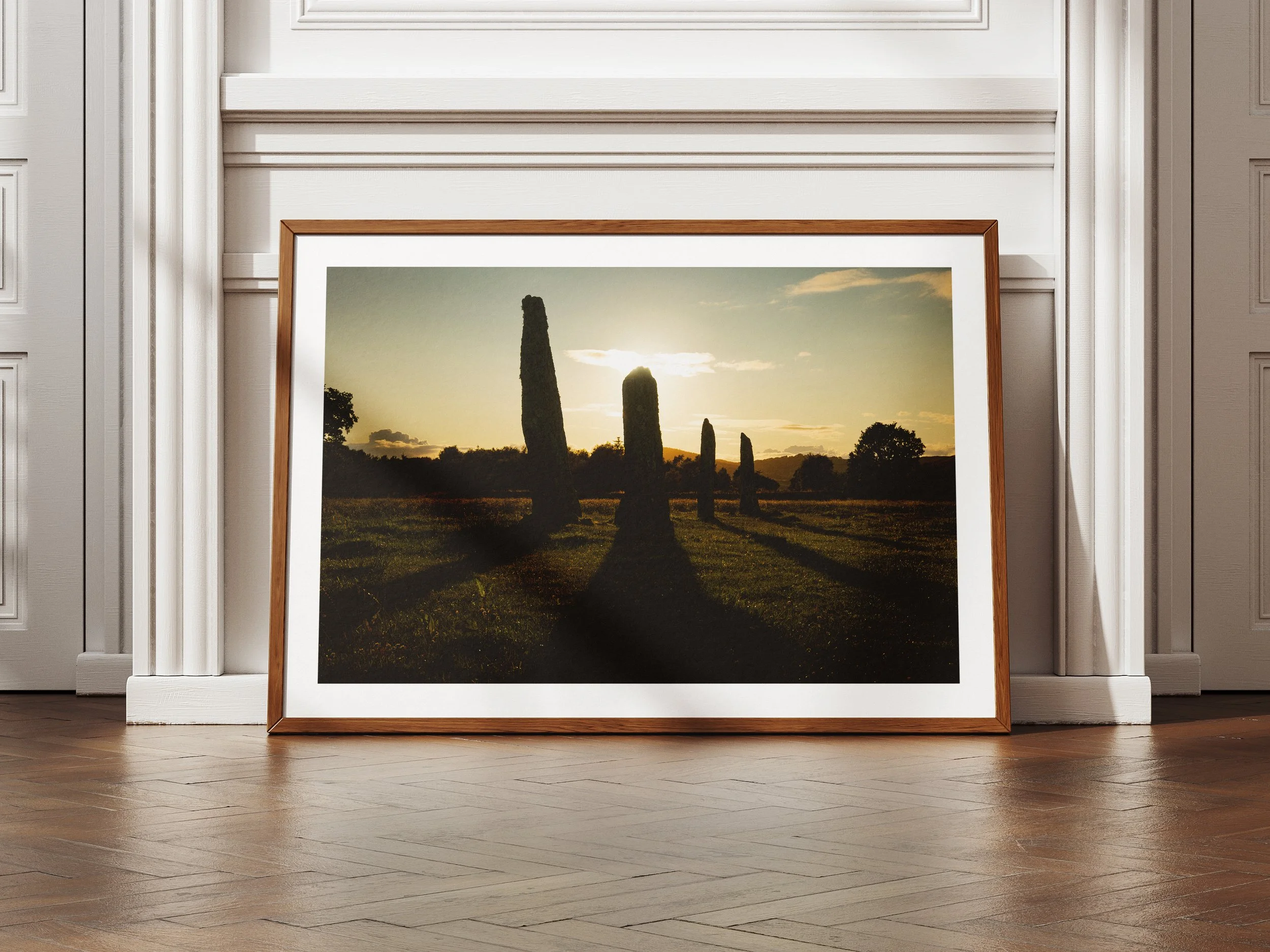 A framed picture of the ballymeanoch stones with the sun setting behind them