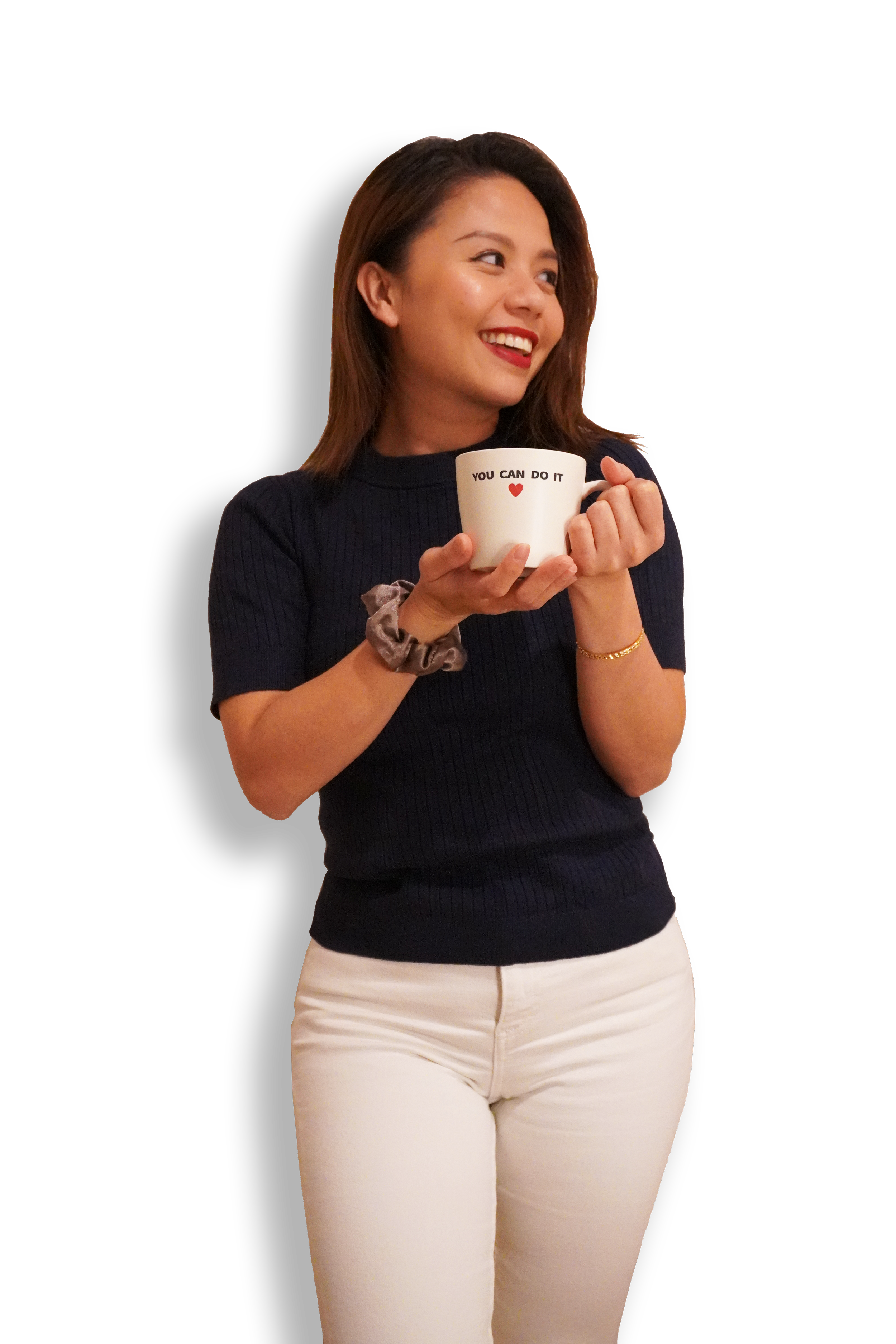 A young woman with shoulder-length brown hair, wearing a black short-sleeved top and white pants, holding a white mug with a motivational message, smiling and looking to her left.