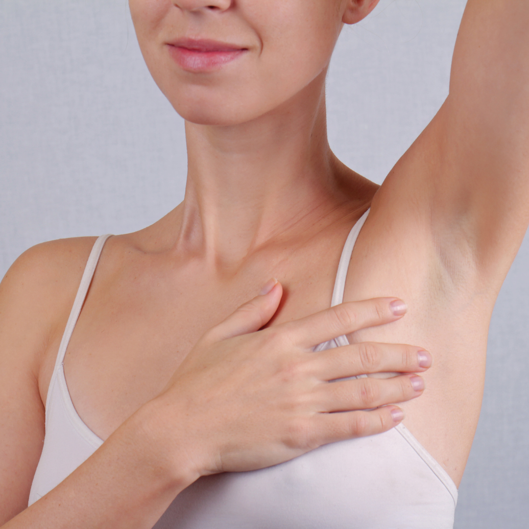 A woman smiling with her hand on her chest and her other arm raised, showing her armpit.