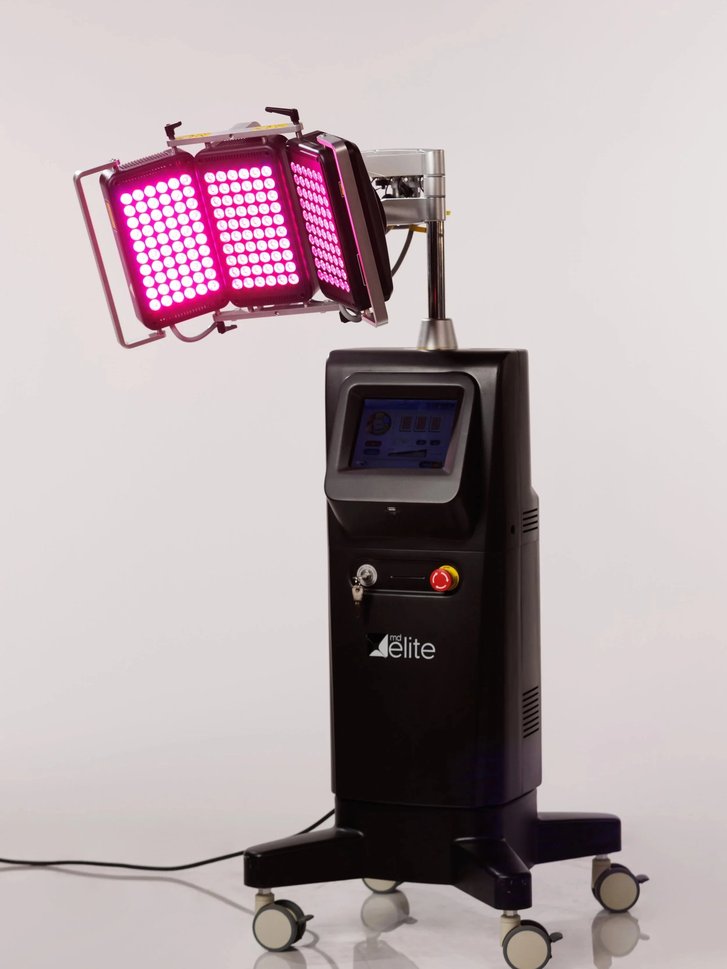 A pink LED light therapy device with three adjustable panels is mounted on a black stand with a touchscreen and control buttons.