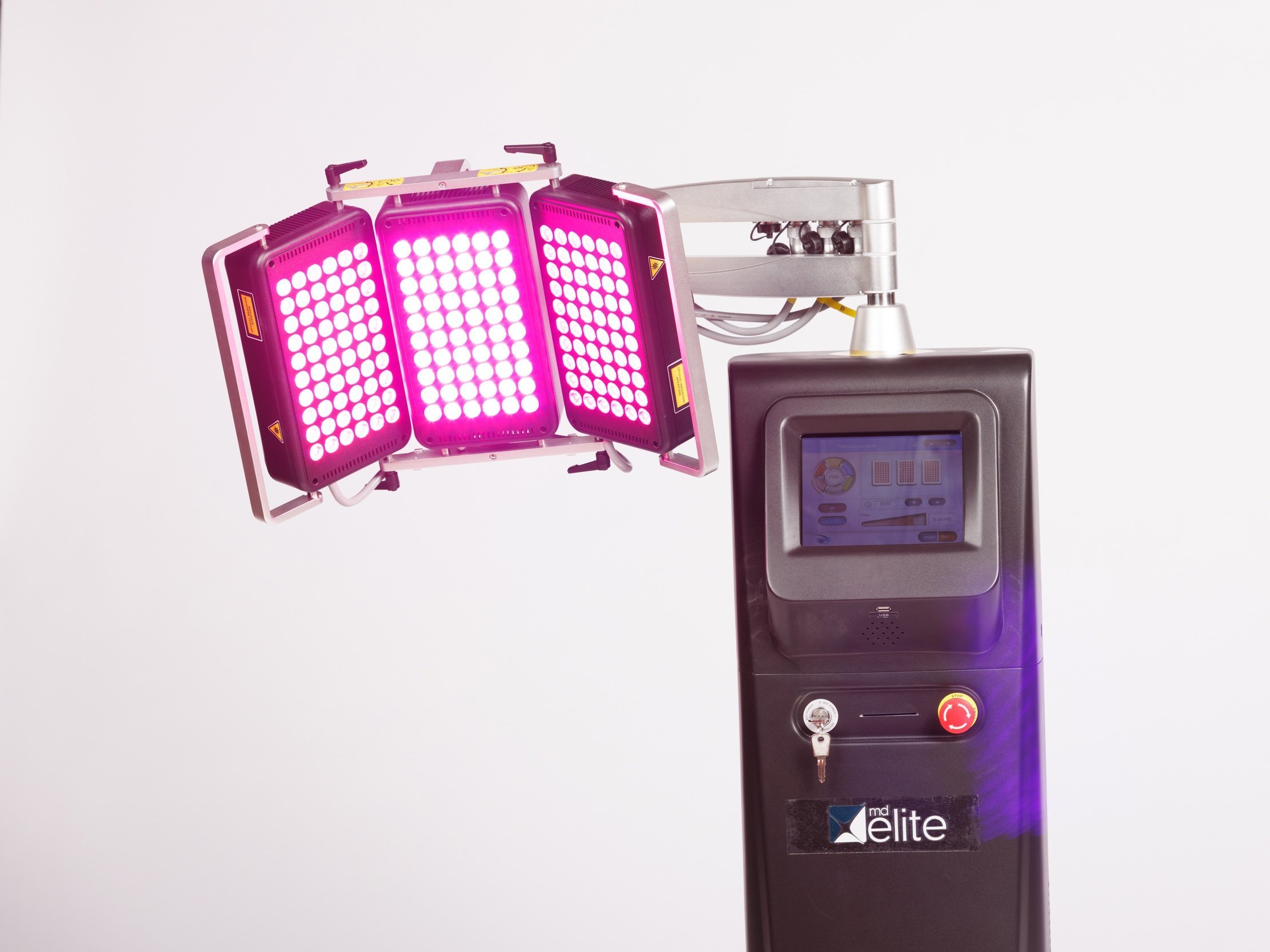 A pink LED light therapy device with three adjustable panels is mounted on a black stand with a touchscreen and control buttons.