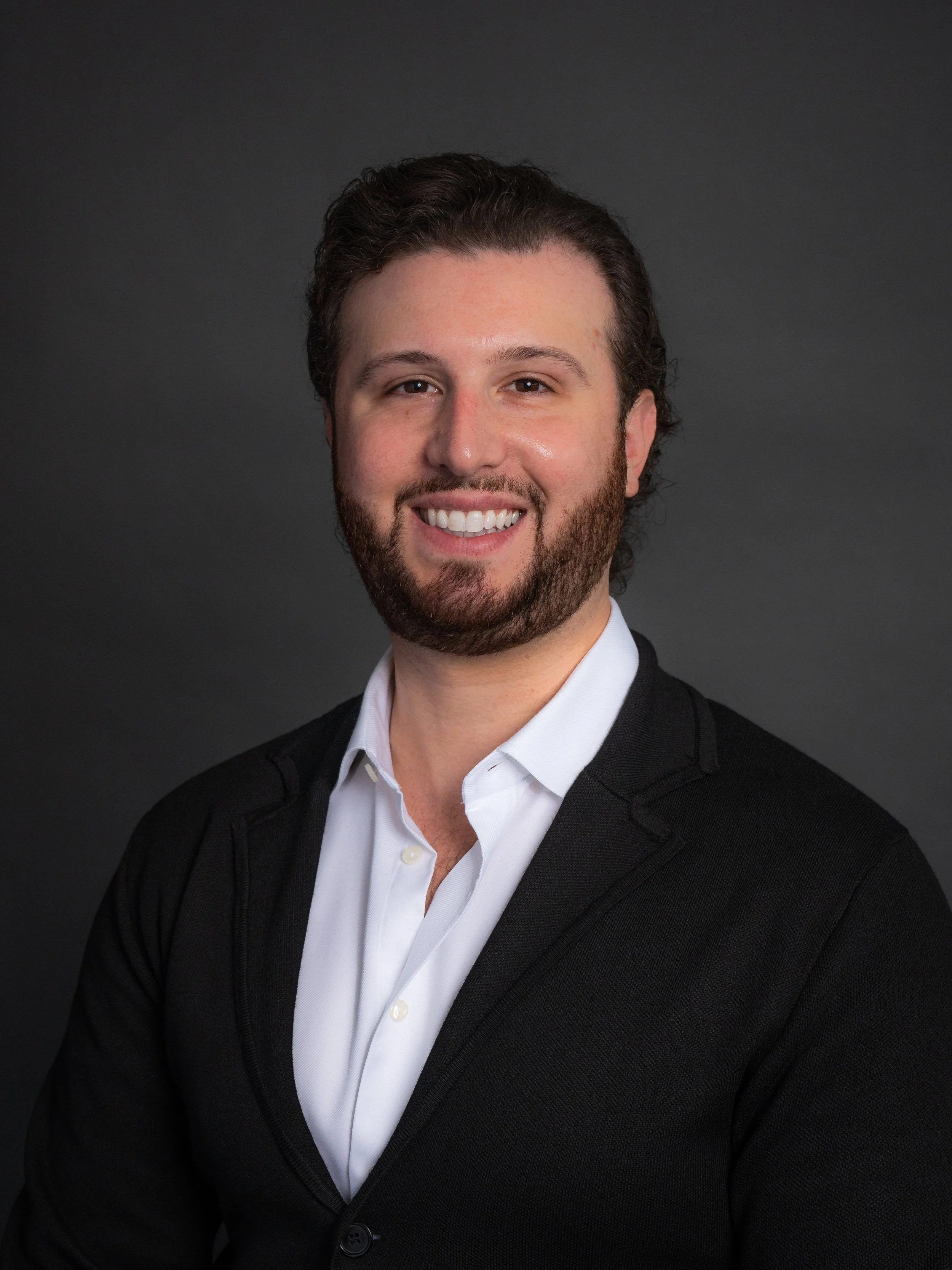 Headshot of VP of Sales Mitch, wearing a white shirt and a black blazer, smiling against a dark background.