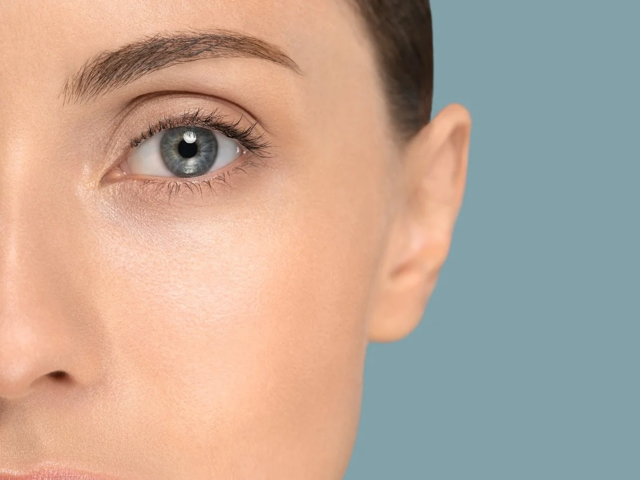 Close-up of a person's face showing their left eye, eyebrow, and part of their cheek and ear, with clear skin and blue eye.