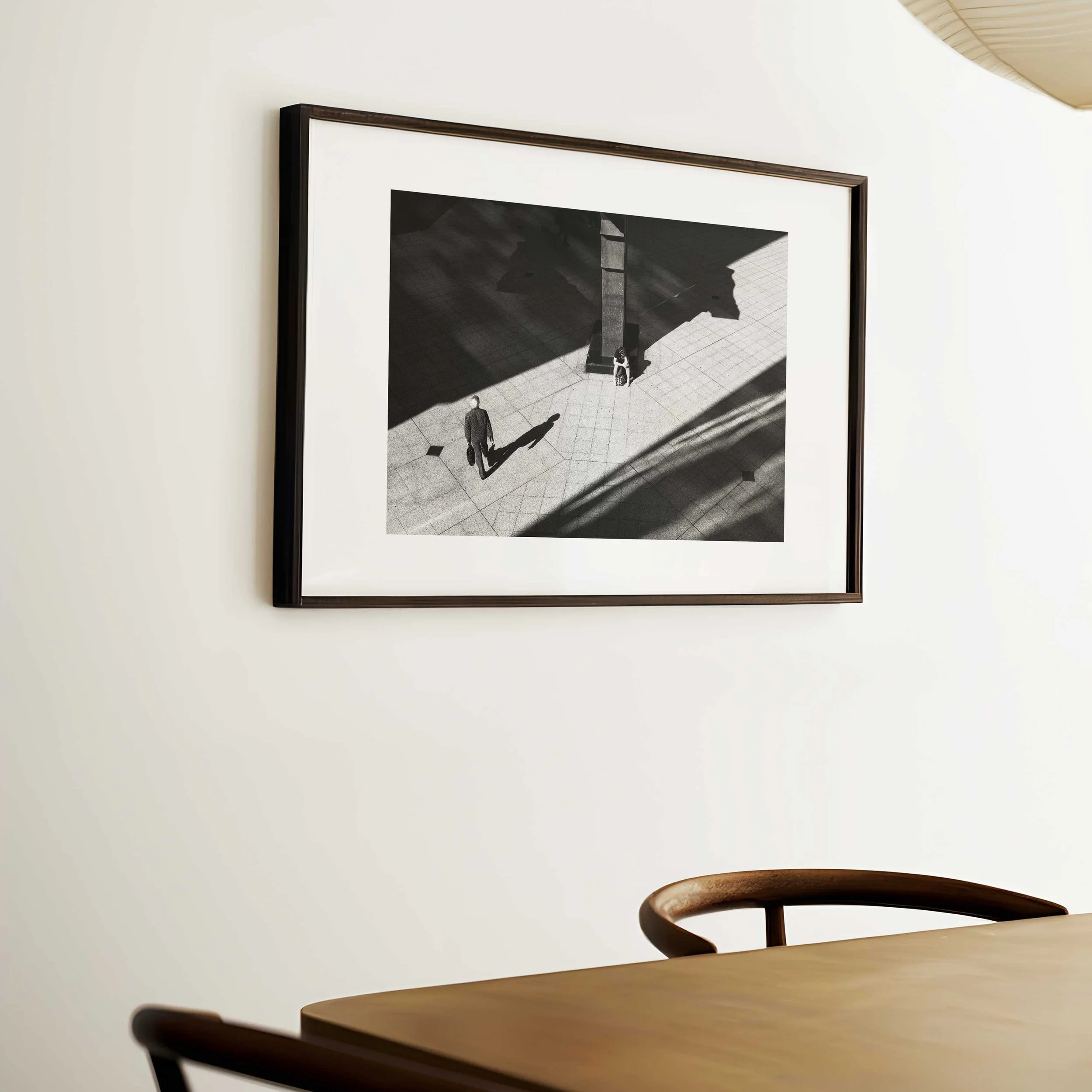 Black and white street photograph of two isolated figures separated by strong geometric shadows and light inside a modern architectural space.