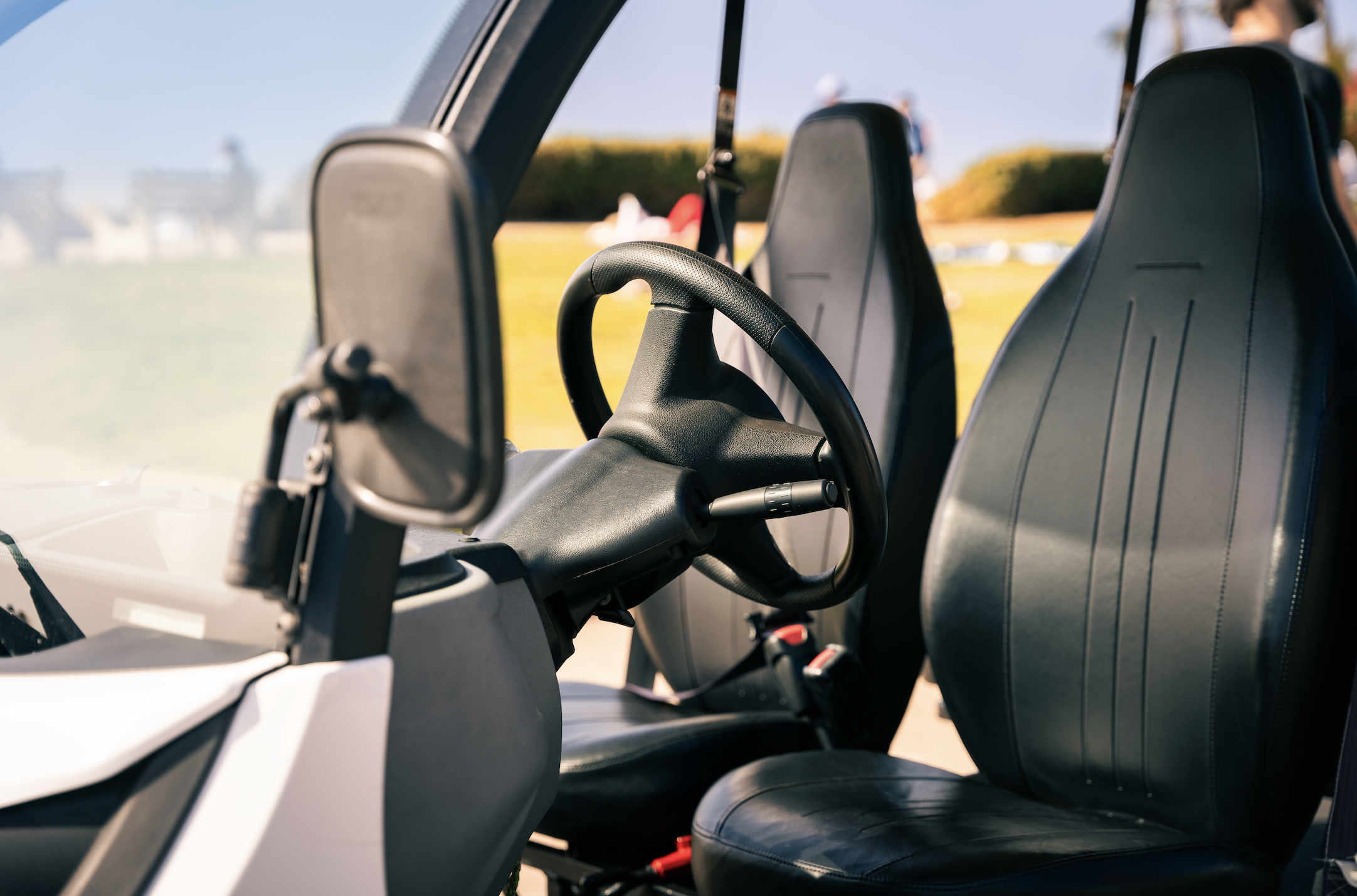 Close-up of the interior of a golf cart, showing the steering wheel, driver and passenger seats, and some background scenery.