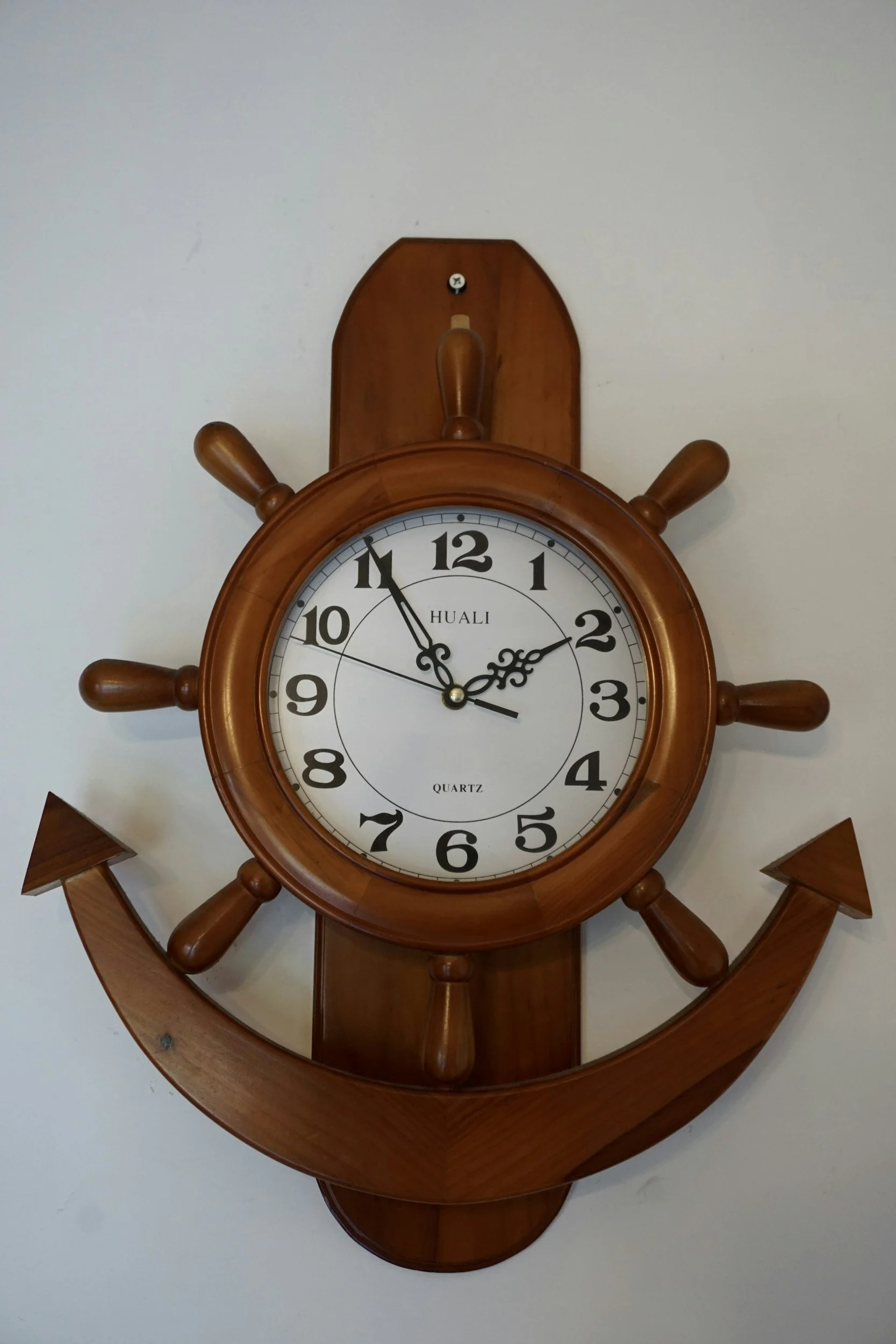 Wall clock designed like a ship's wheel and anchor, wooden frame, white face, black numerals, and hands showing 2:57.