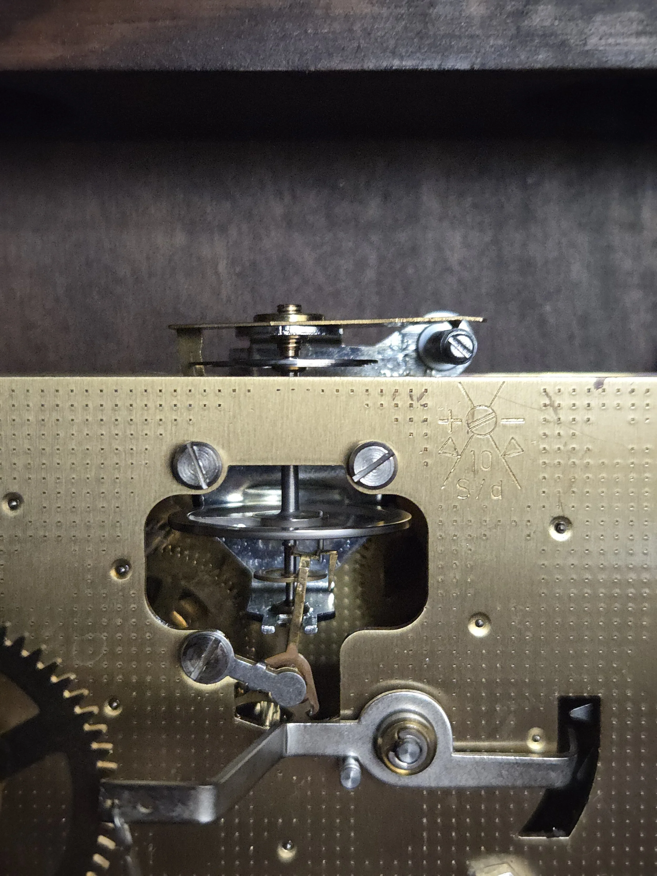 Close-up of the inner mechanical components of a clock, showing gears, screws, and metal parts.