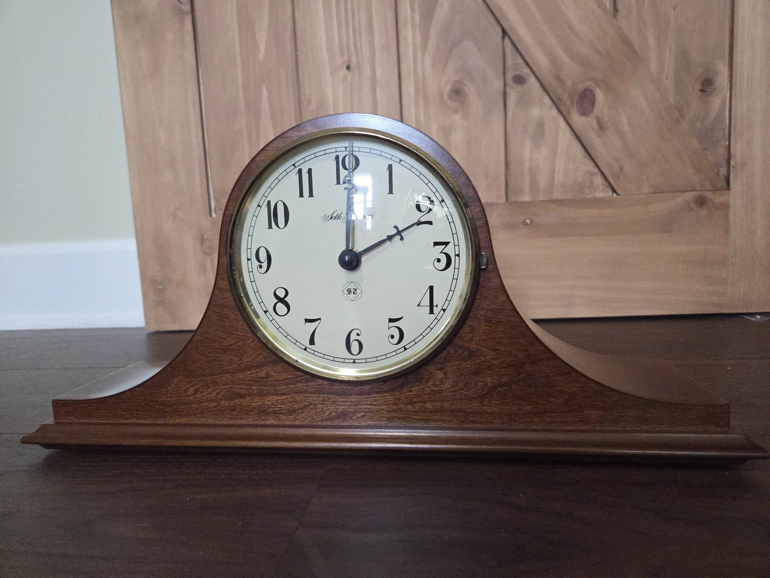 A wooden mantel clock showing the time as 12:10.