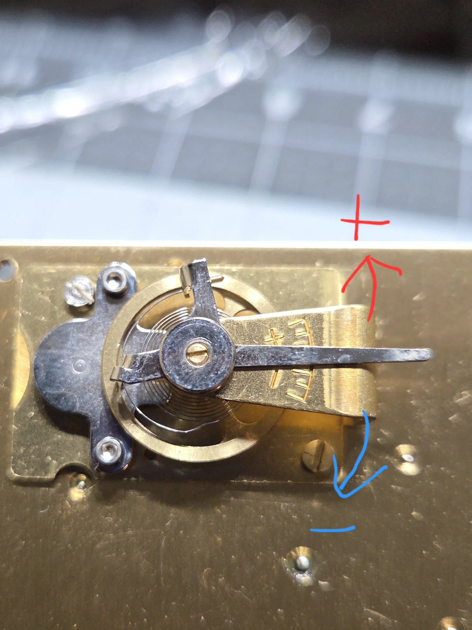 Close-up of a clock's internal mechanism showing a gear and metal components, with red and blue arrows drawn on the image pointing in different directions.