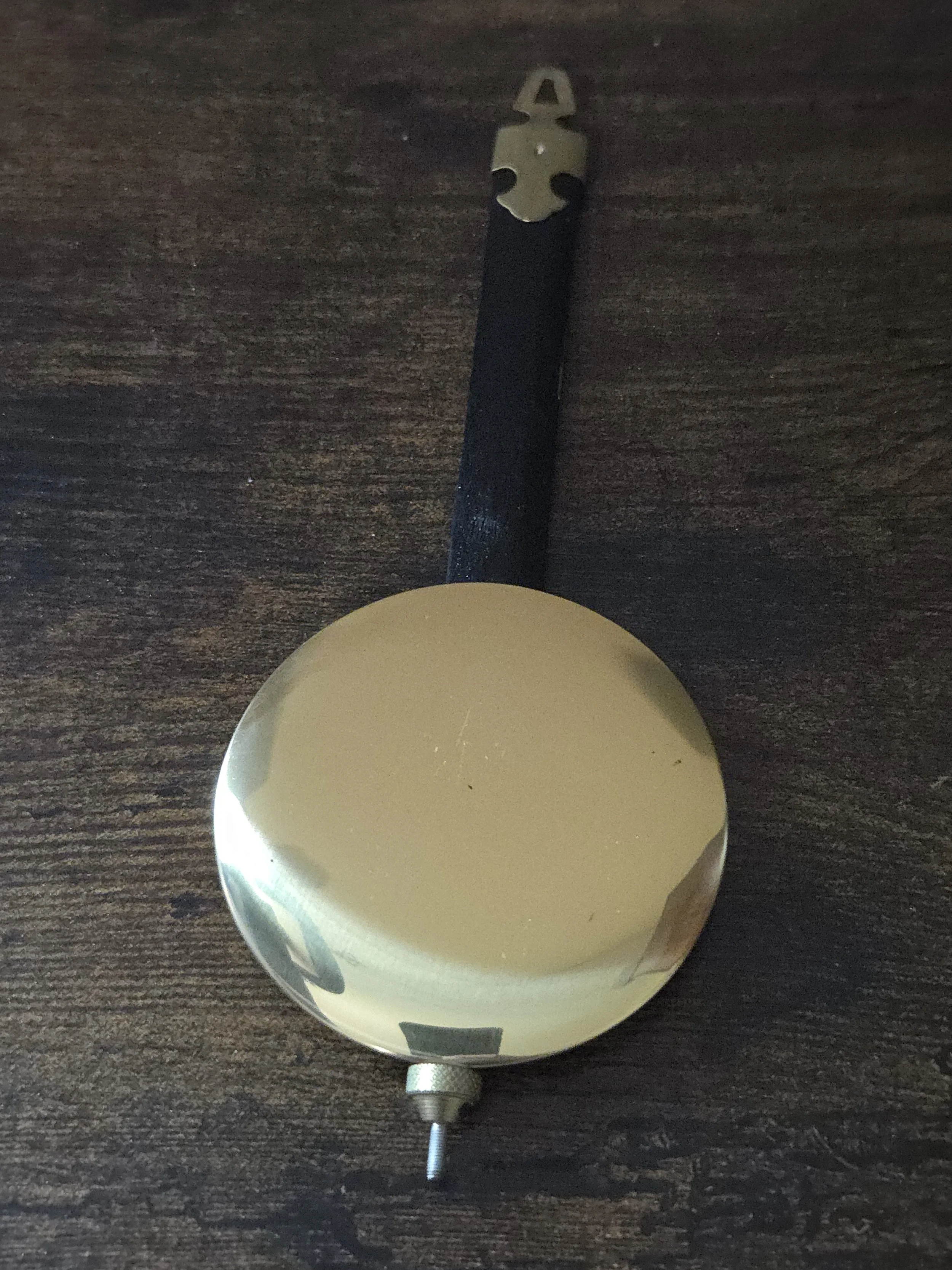 A vintage metal alarm clock with a round face, no visible hands, and a black strap attached to a metal clip, lying on a wooden surface.