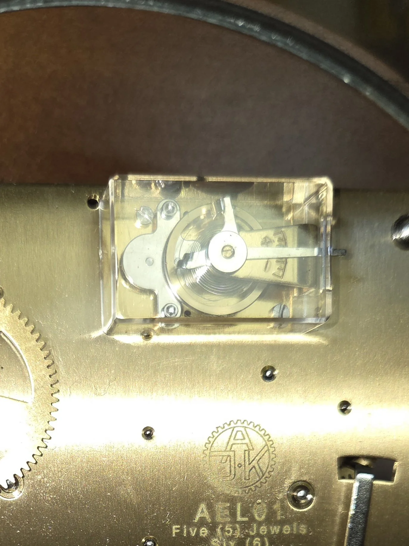Close-up of a clock's inner mechanism with gears and a small transparent case showing a part of the clock's movement.