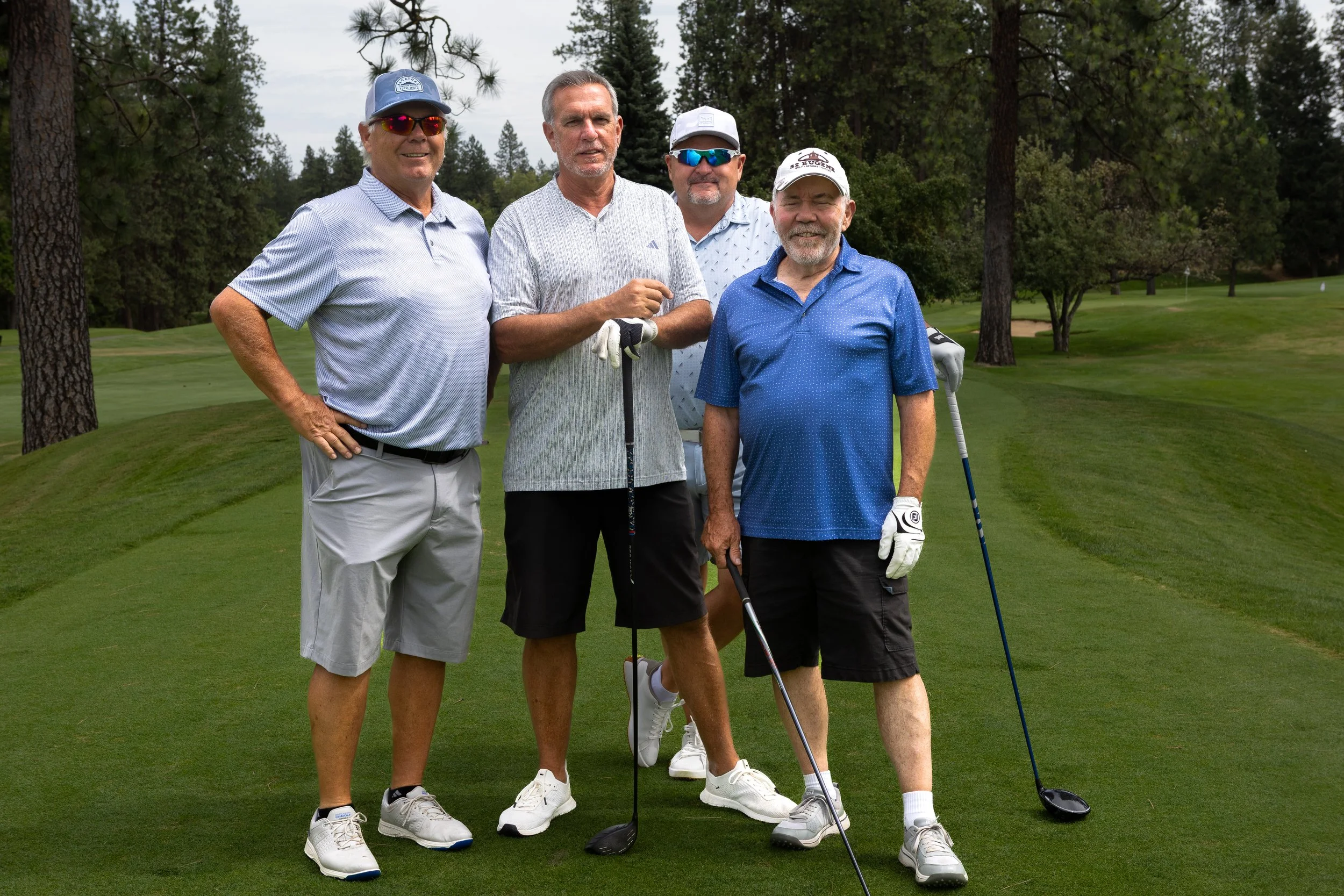 Group of four men in golf attire holding a golf club.