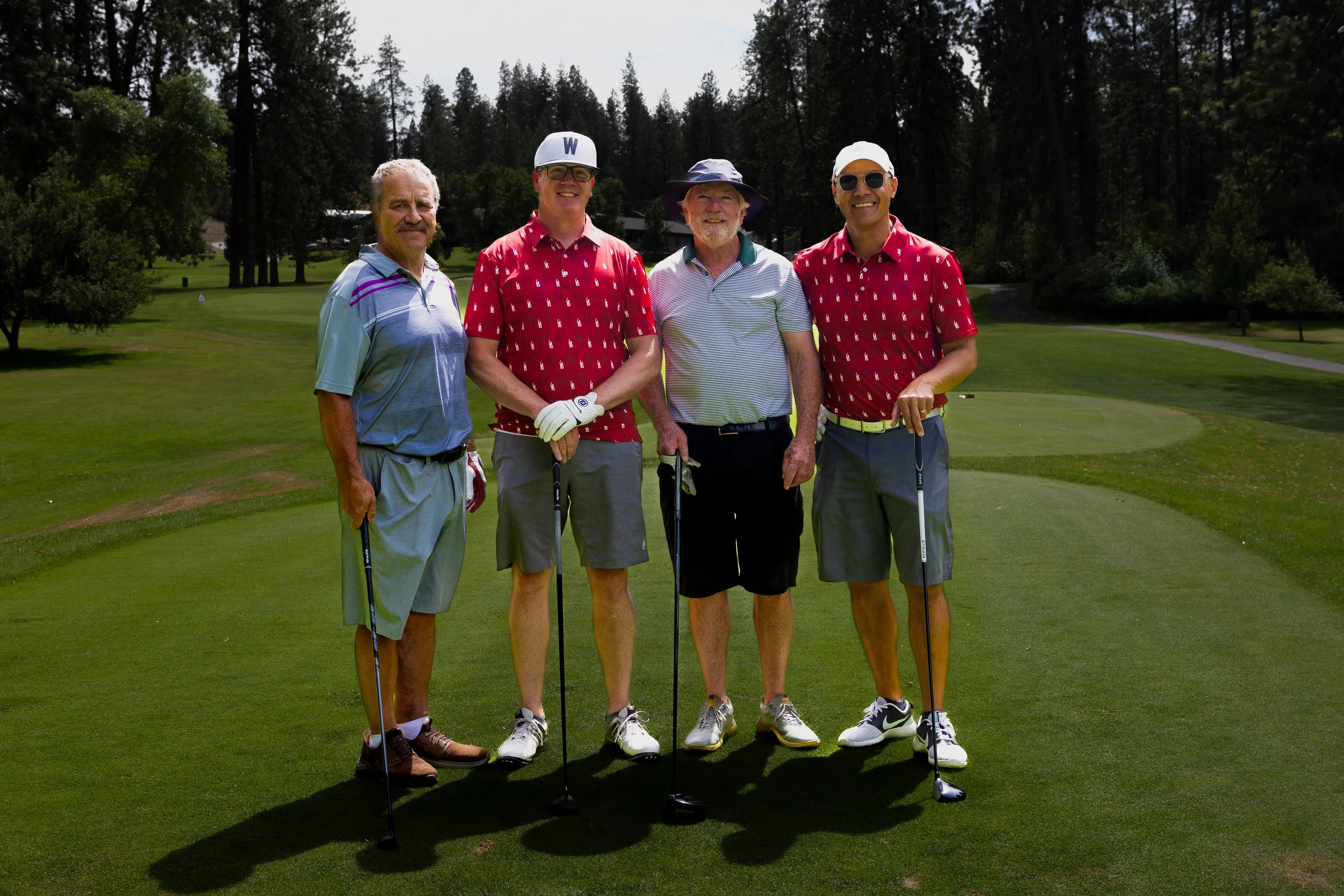Four people in golf attire standing for a picture holding a golf club