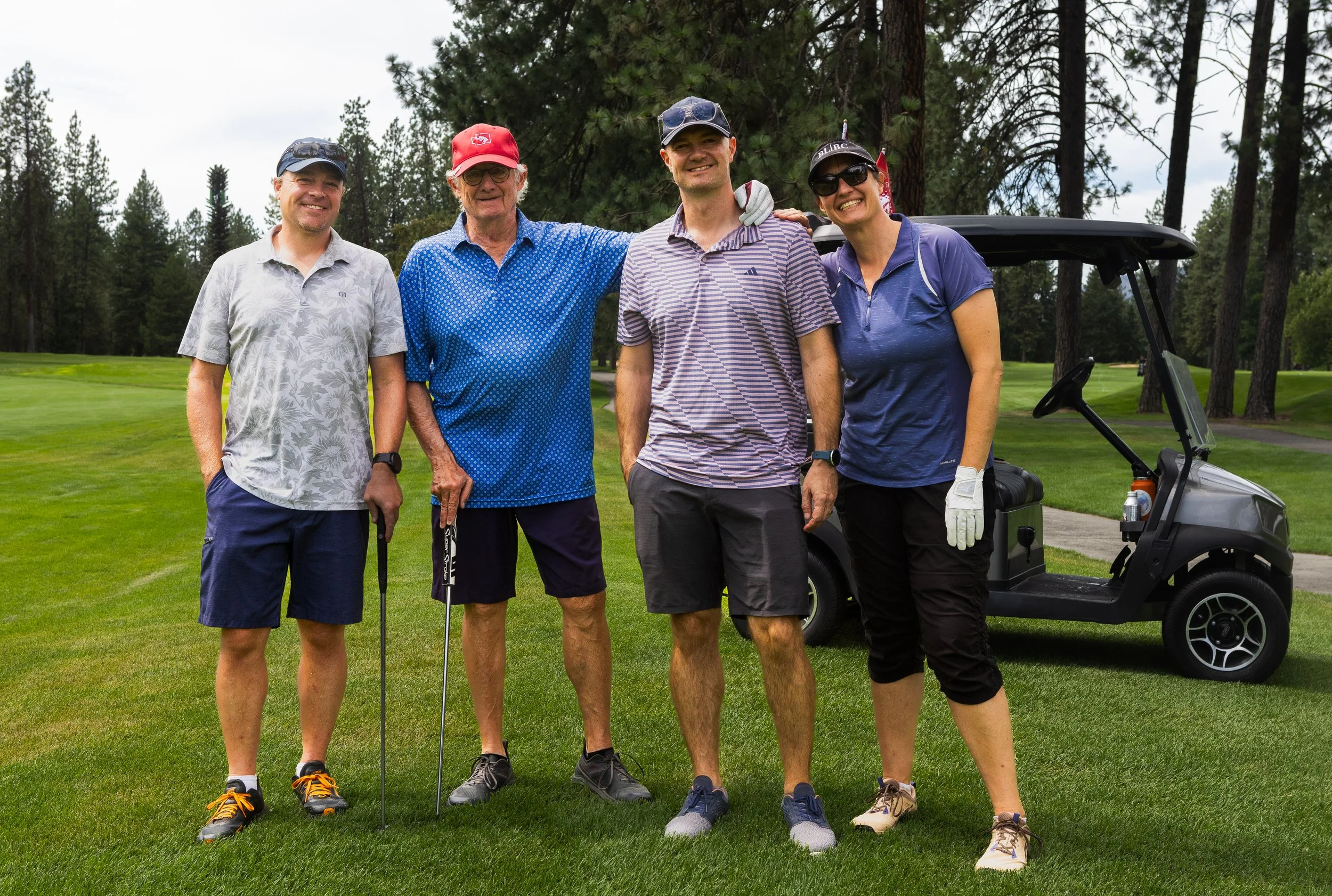 Four people in golf attire with a golf cart in the background
