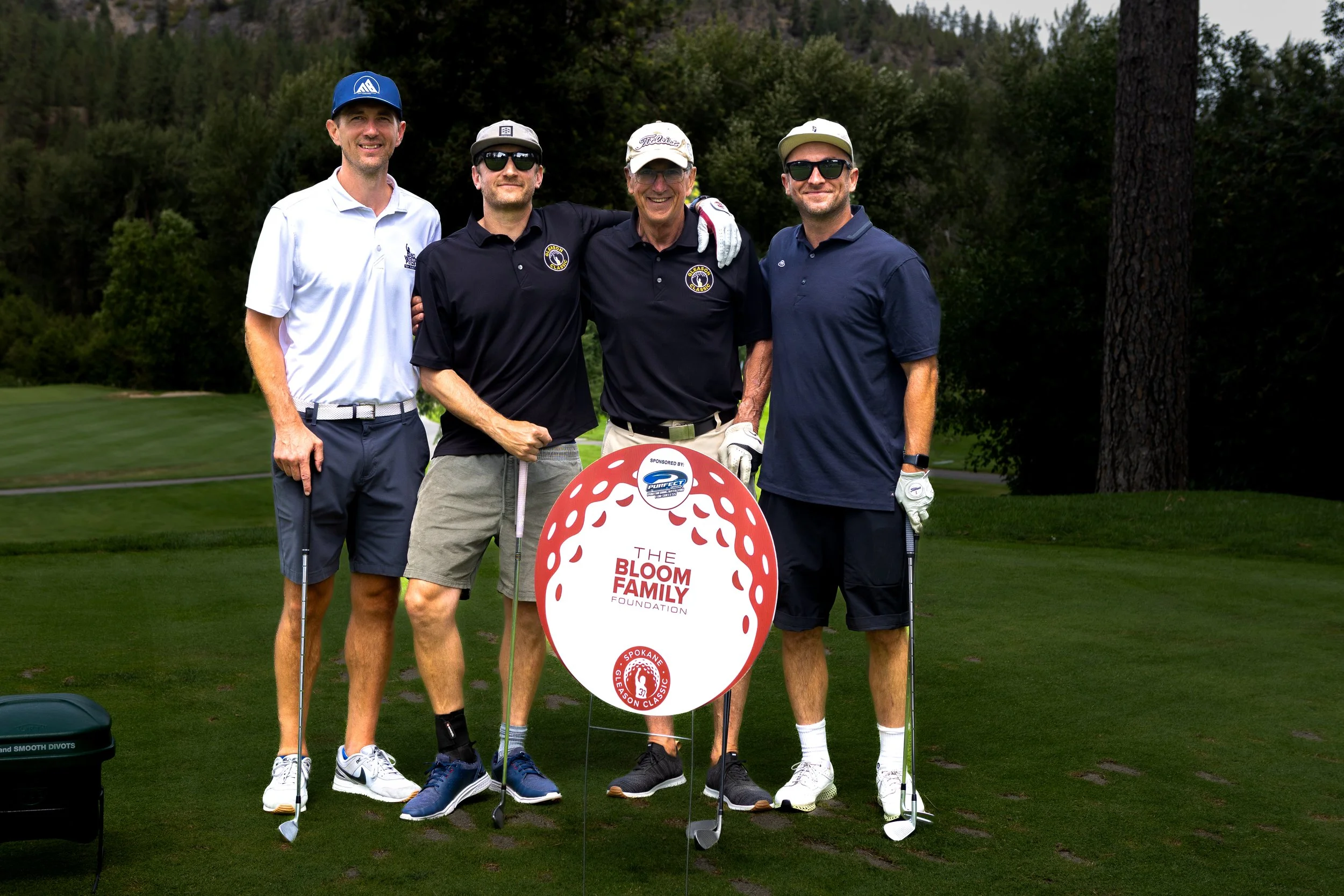 Four men in golf attire standing with a marker sign that says The Bloom Foundation