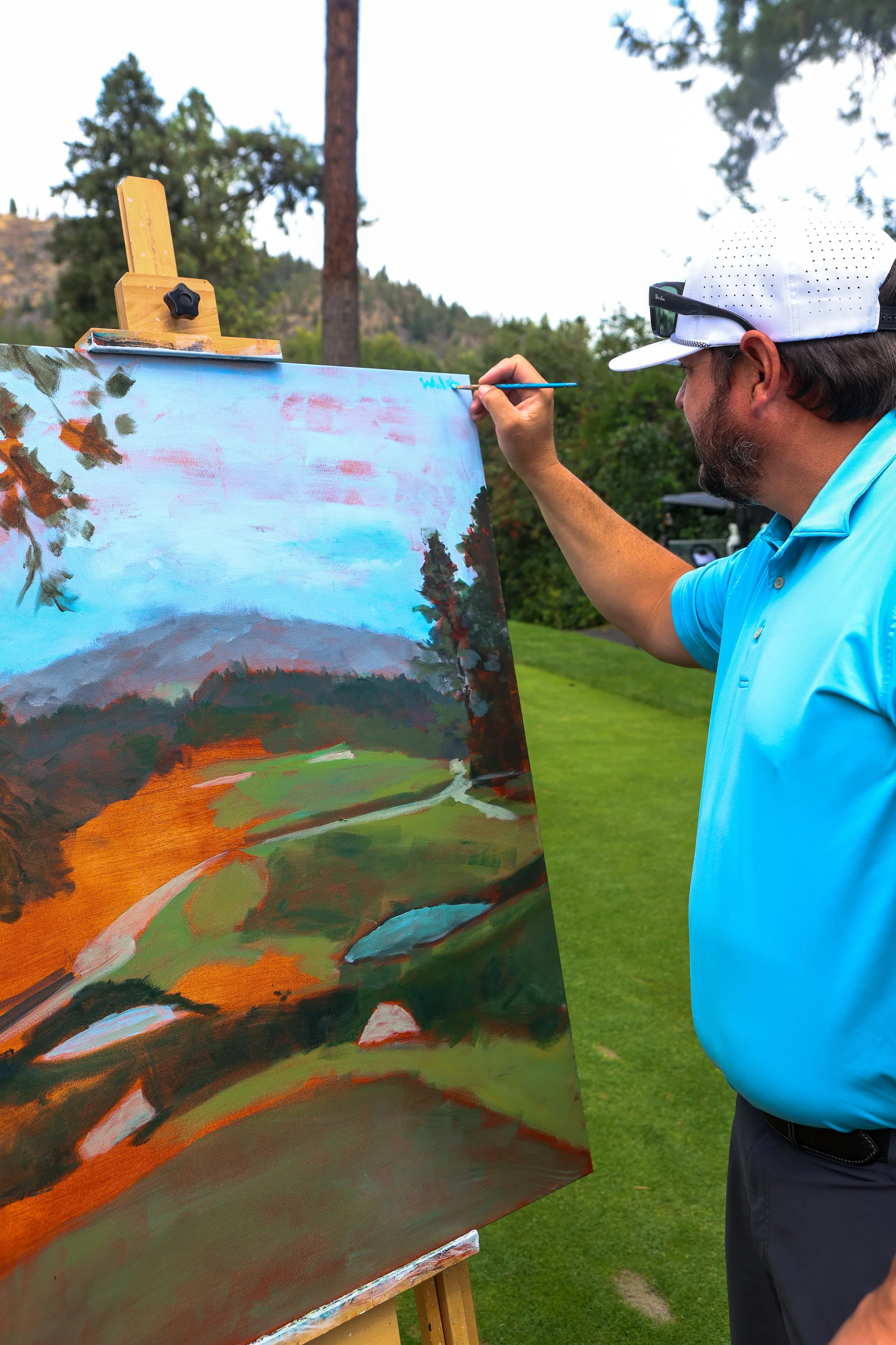 Close up of a painted picture and a person signing their initials on the painting