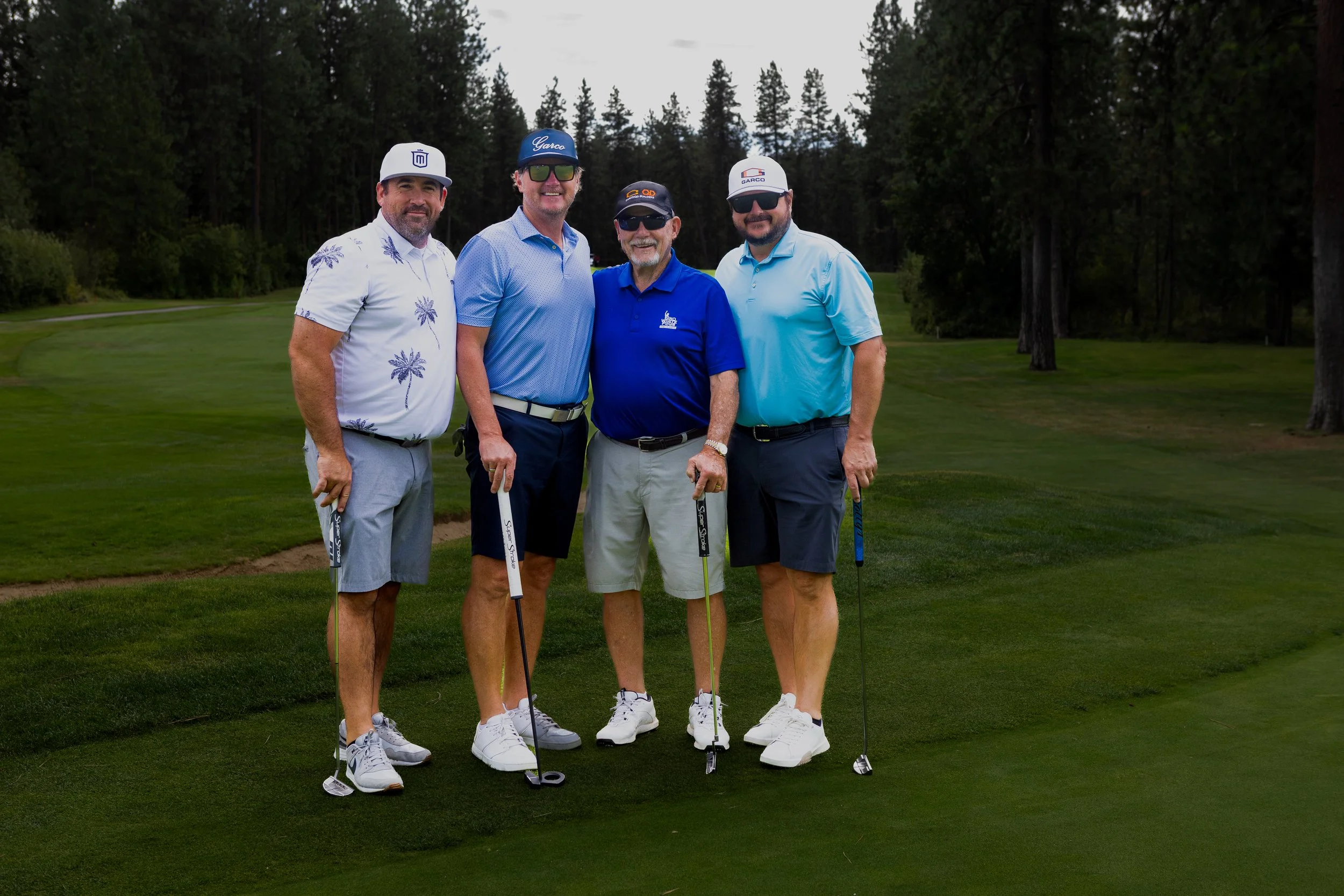 Four men in golf attire standing for a photo on the golf course