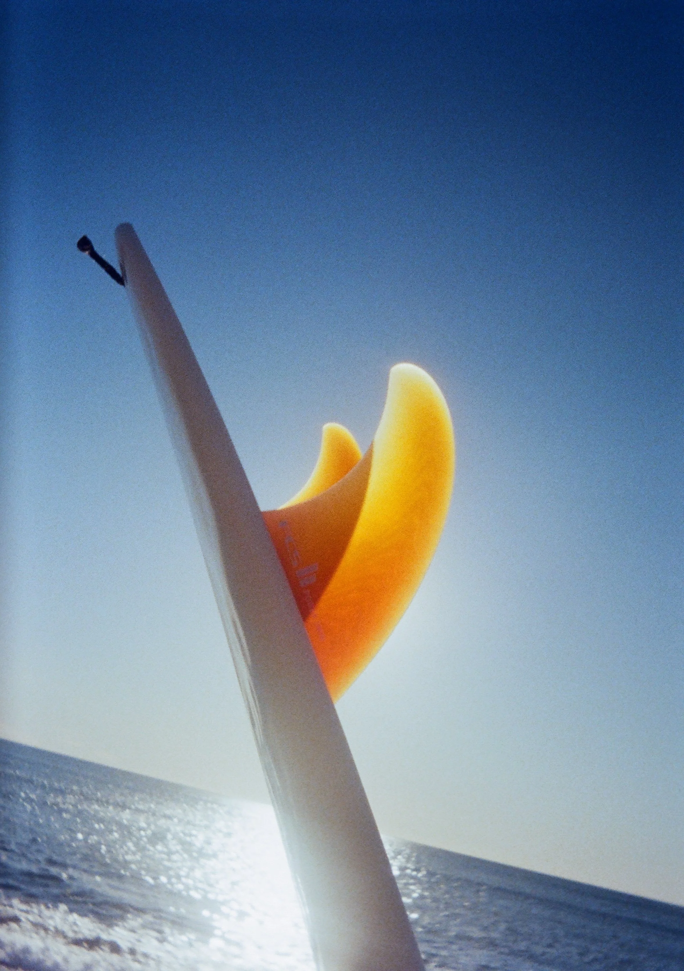 A glowing, yellow inflatable object at the beach with a white device, possibly a surfboard, next to it, under a clear blue sky.