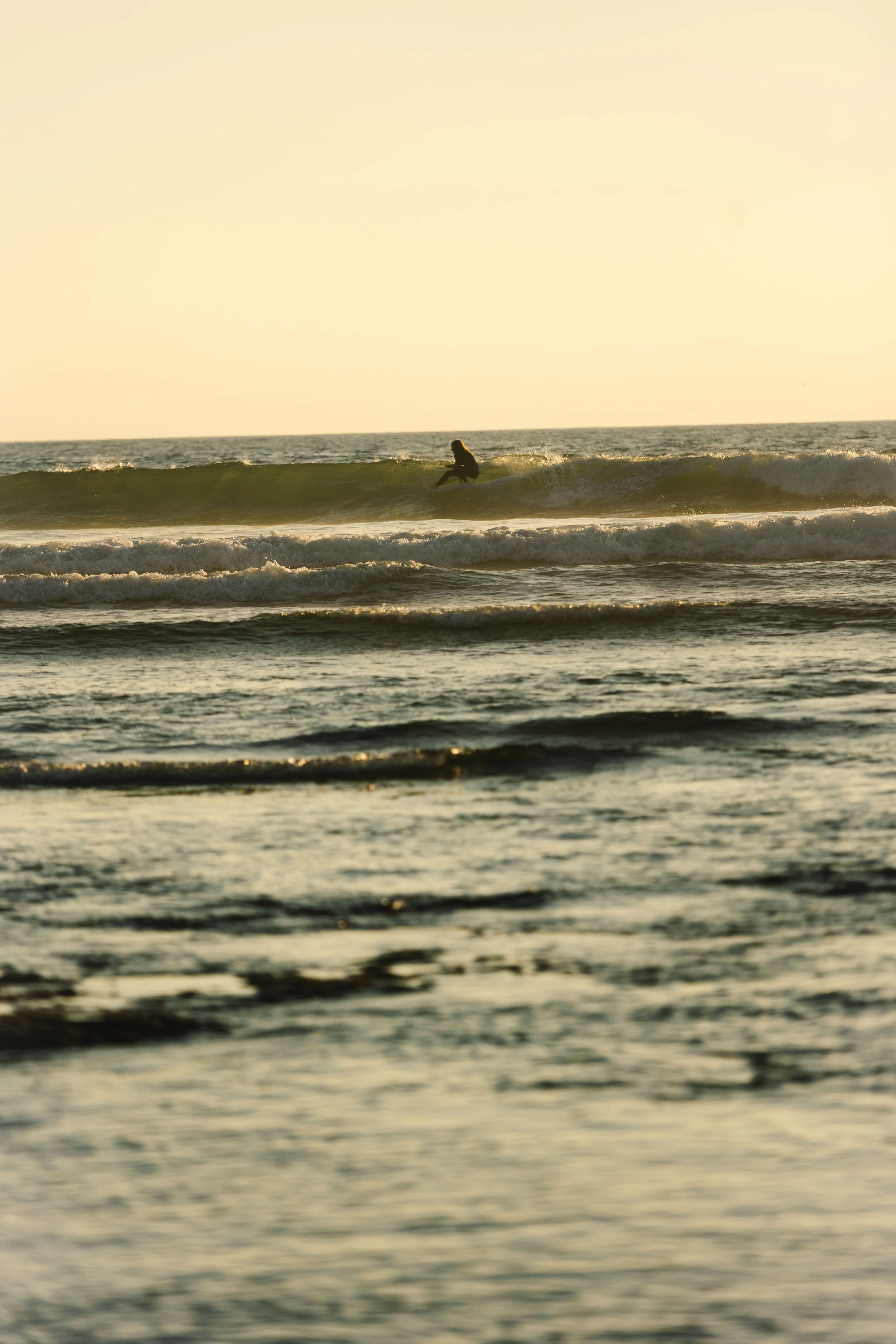 A person surfing on a wave in the ocean during sunset.