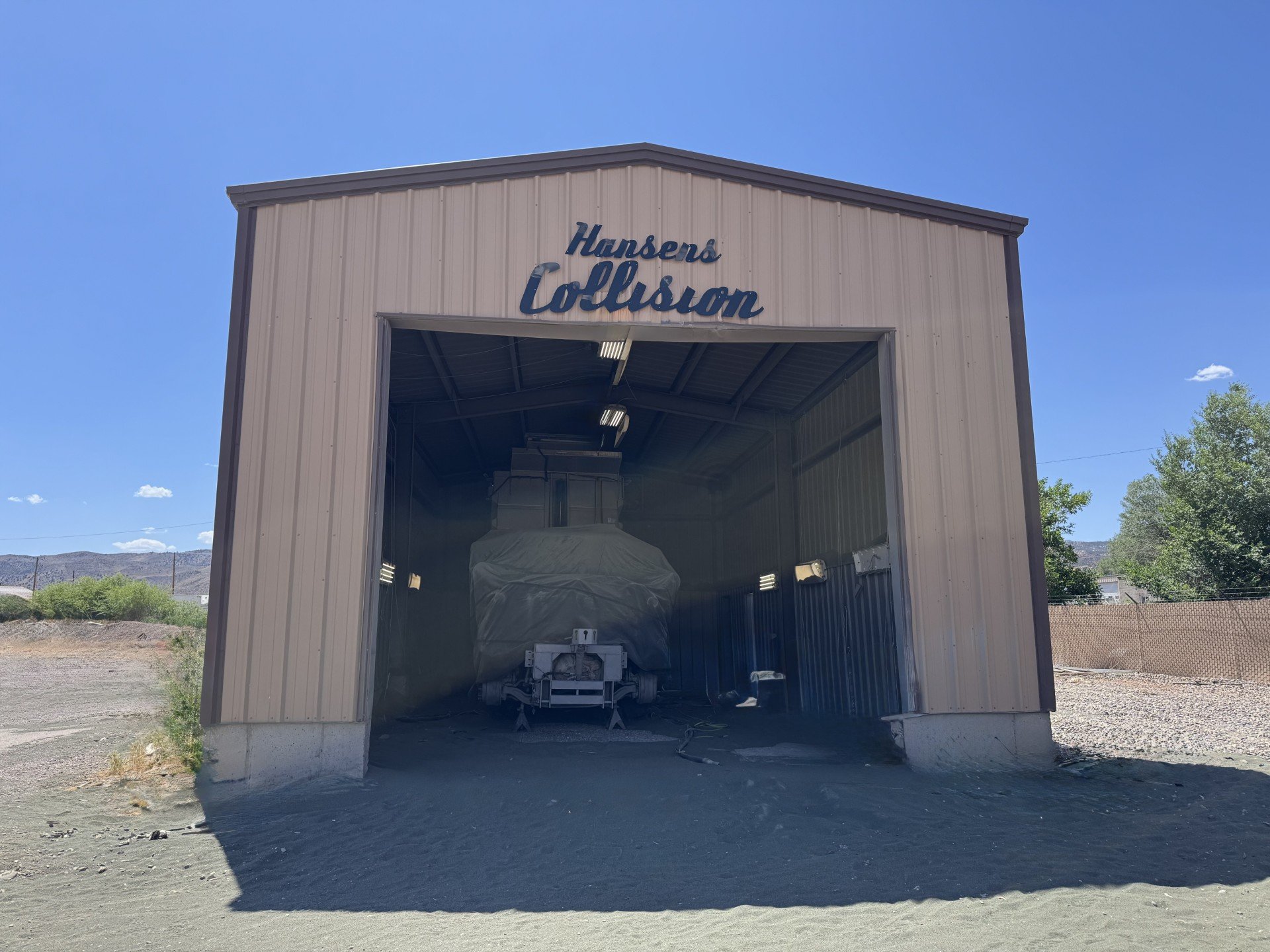 A metal storage building with the sign "Hansens Collision" on the front. Inside, a covered vehicle is visible, ready to be sandblasted.