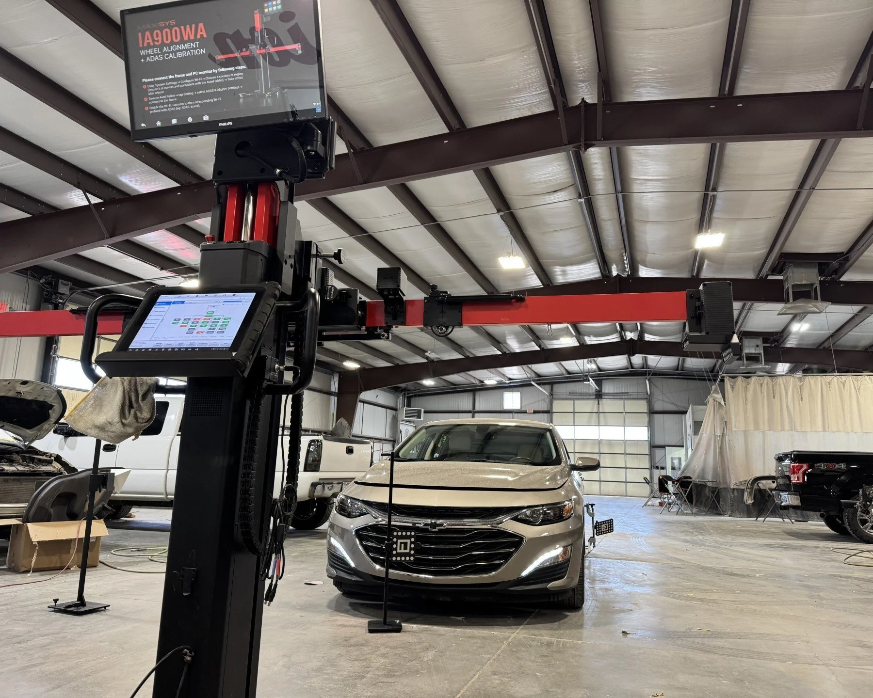 Automotive calibration machine in a our shop, with a silver car positioned in front of it, surrounded by tools and equipment.