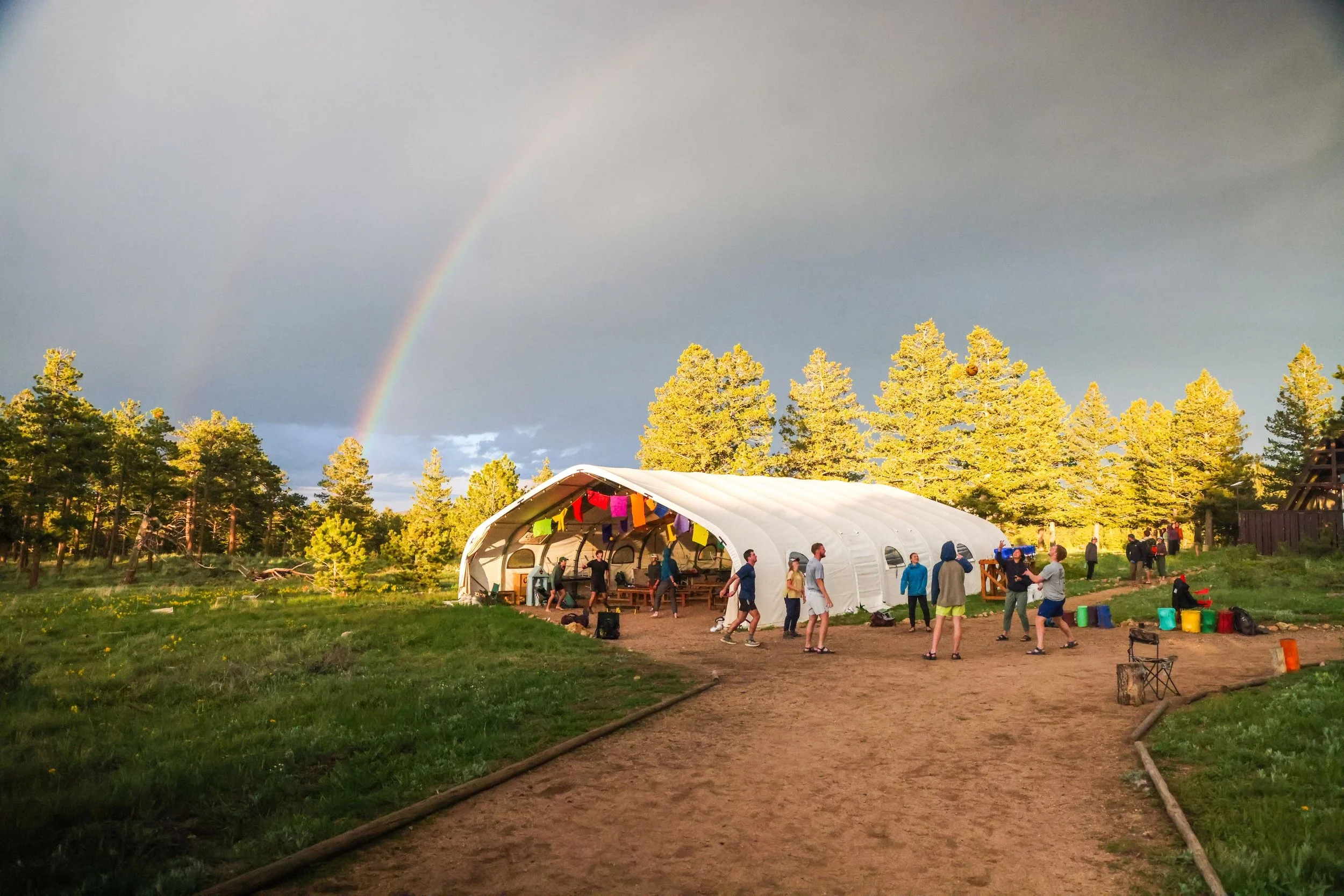 base camp structure at camp wojtyla with people playing outside while a rainbow is in the sky