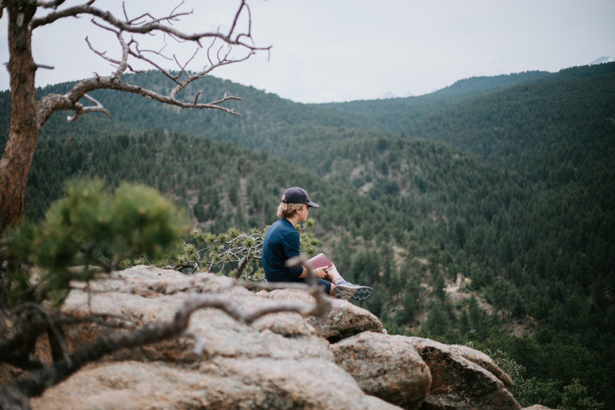 middle school boy sitting on edge looking out over the mountains