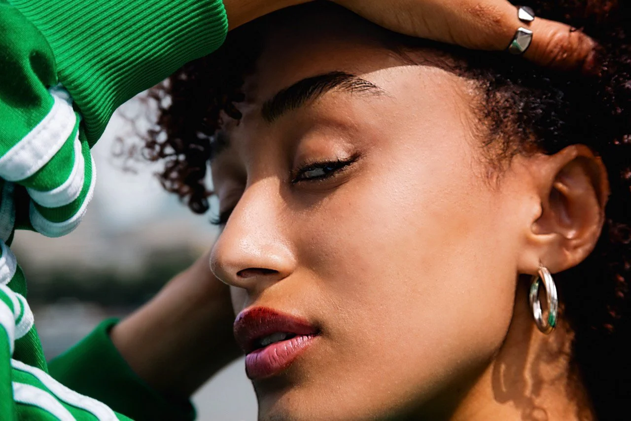 Close-up of a woman with natural curly hair, wearing hoop earrings, with her eyes partly closed and lips slightly parted.