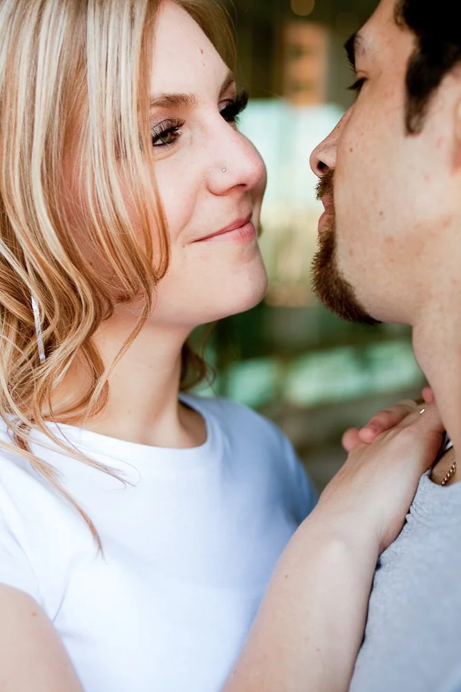 A woman with blonde hair and a nose piercing smiling at a man, with their faces close together in an intimate moment.