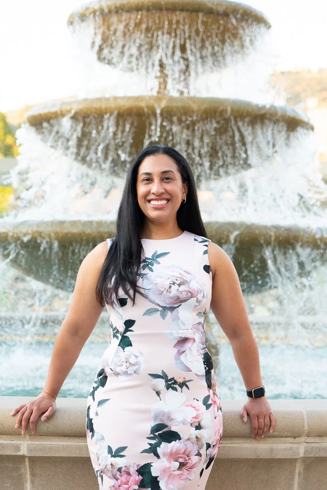 A woman in a floral dress smiling in front of a large, tiered water fountain.